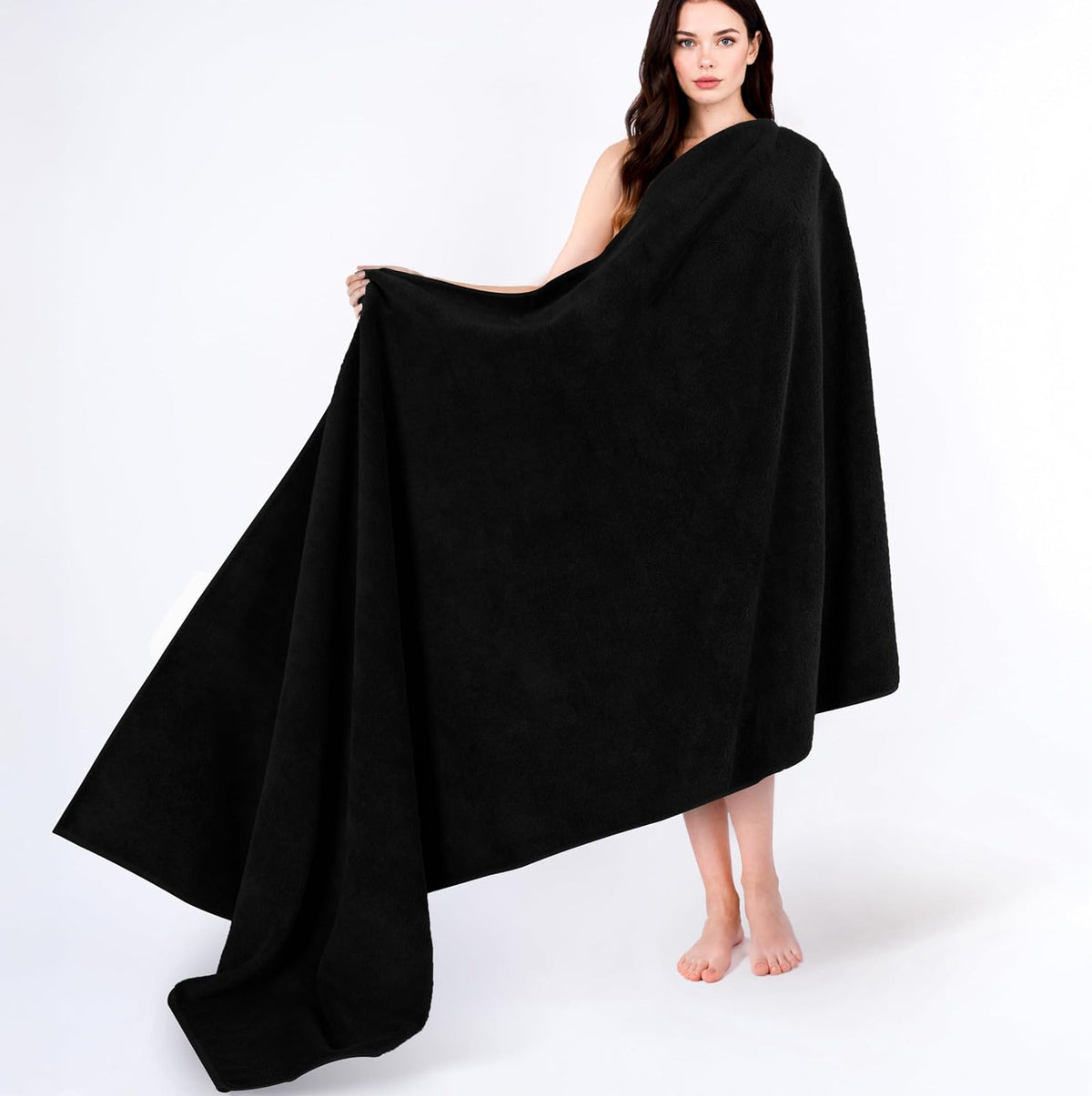 Woman draped in a large black towel, standing barefoot on a seamless white background.