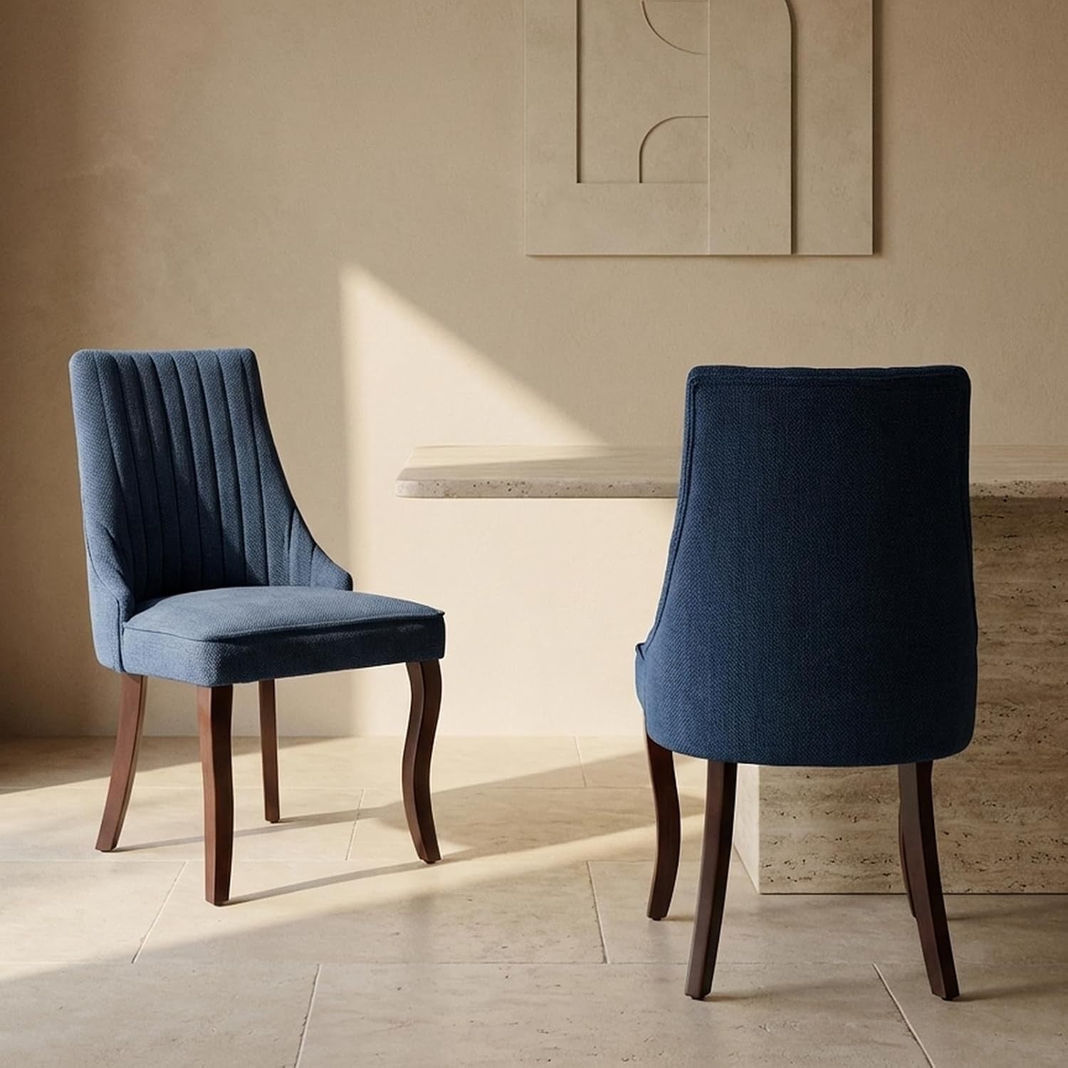 Two navy-blue upholstered dining chairs with vertical channeling and dark wooden legs next to a table.