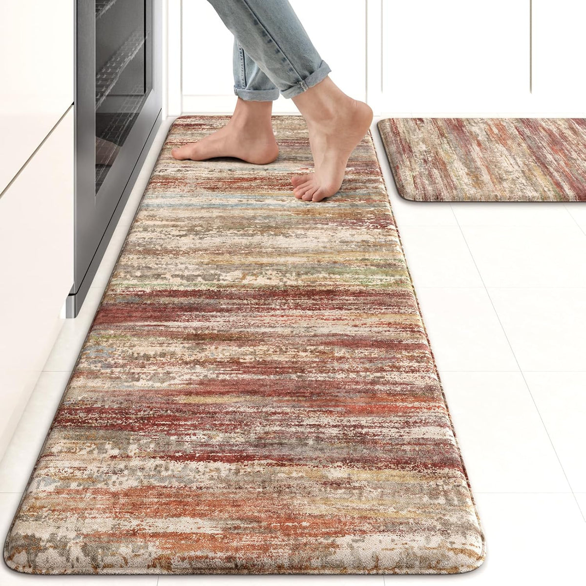 Close angled view of a long rust-and-earth-toned kitchen mat with bare feet standing on it.
