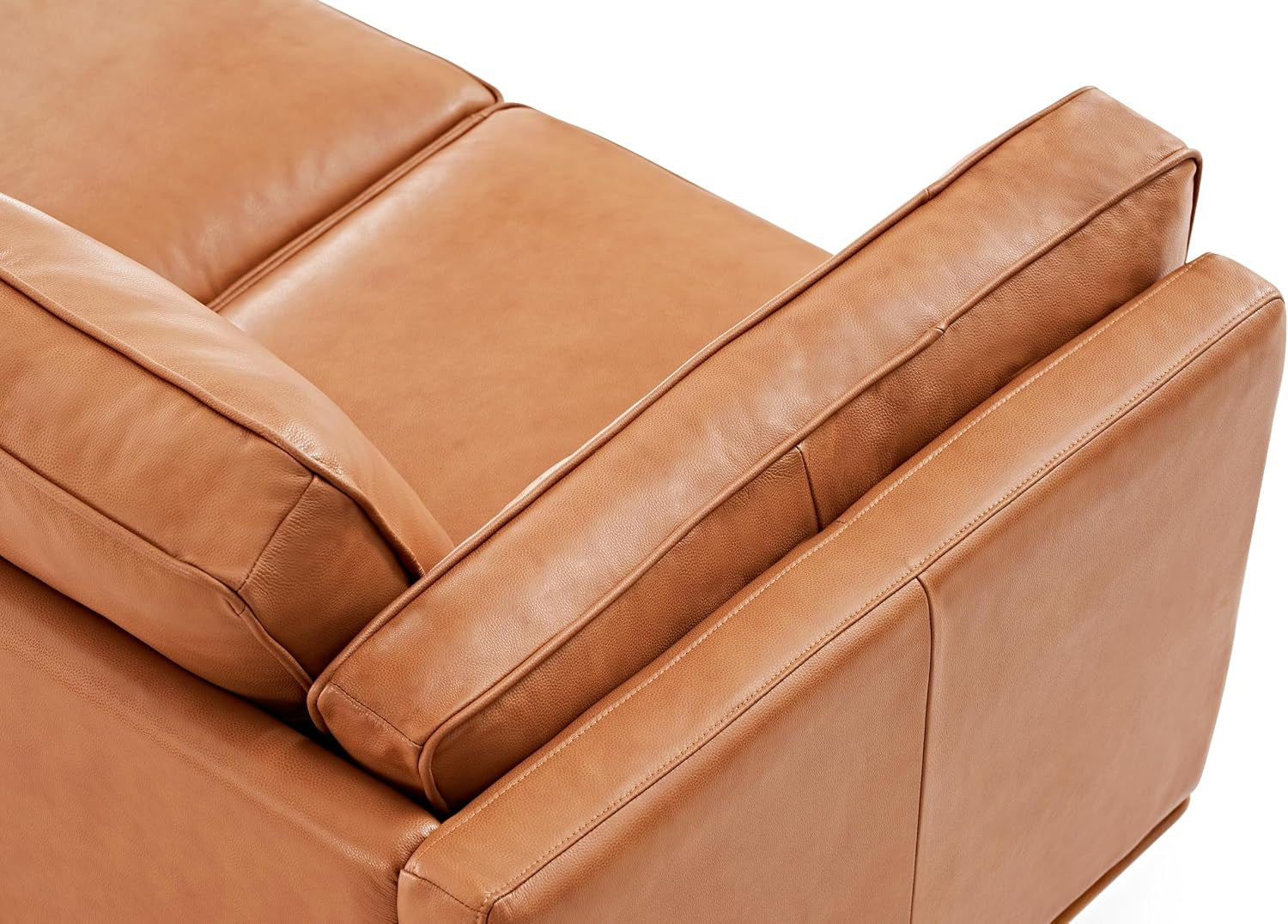 Close-up of a cognac leather sofa's back cushion and corner arm with visible piping.