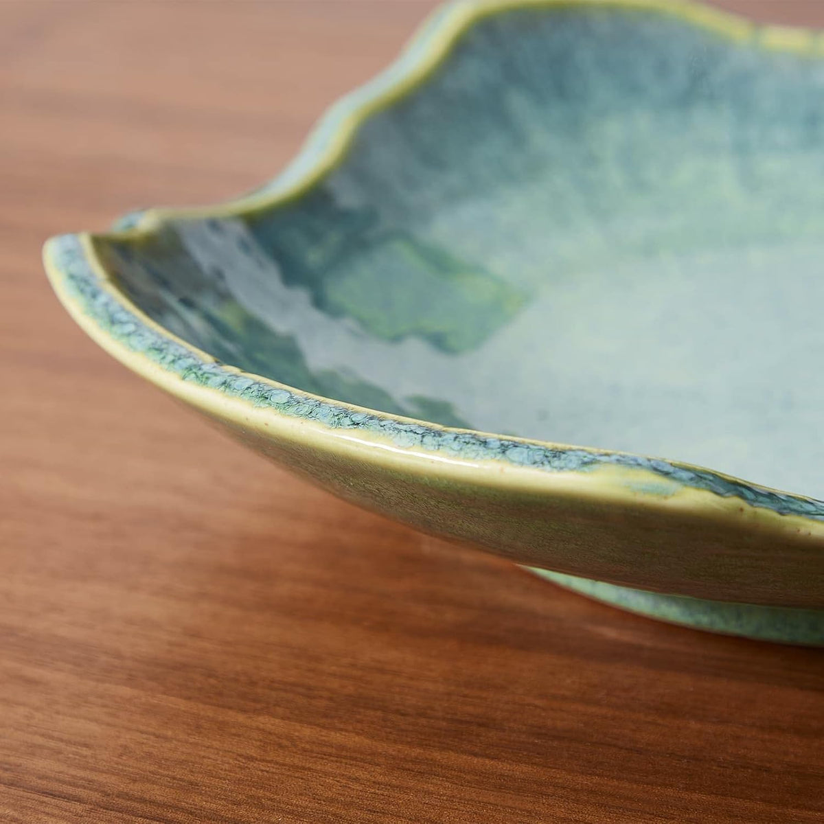 Close-up of the bowl's scalloped rim and crackled green glaze resting on a wood surface