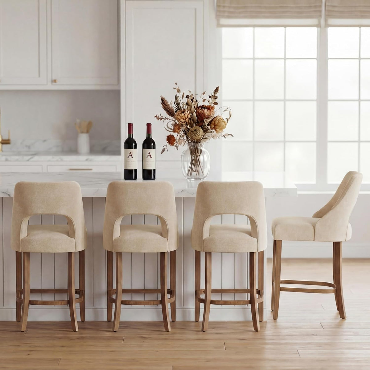 Rear view of four beige counter stools lined at an island showing curved back cutouts and vase on countertop