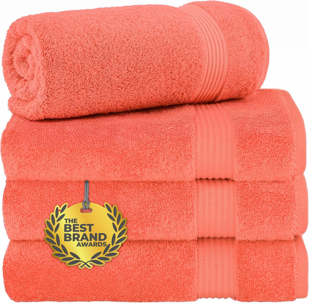 Three coral towels stacked with a rolled towel on top, showing ribbed bands and plush terry texture.