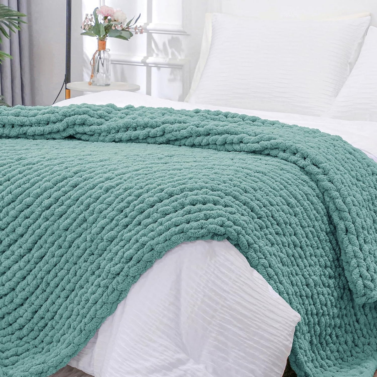 Close view of a seafoam green chunky knit throw folded over the edge of a white bedspread.