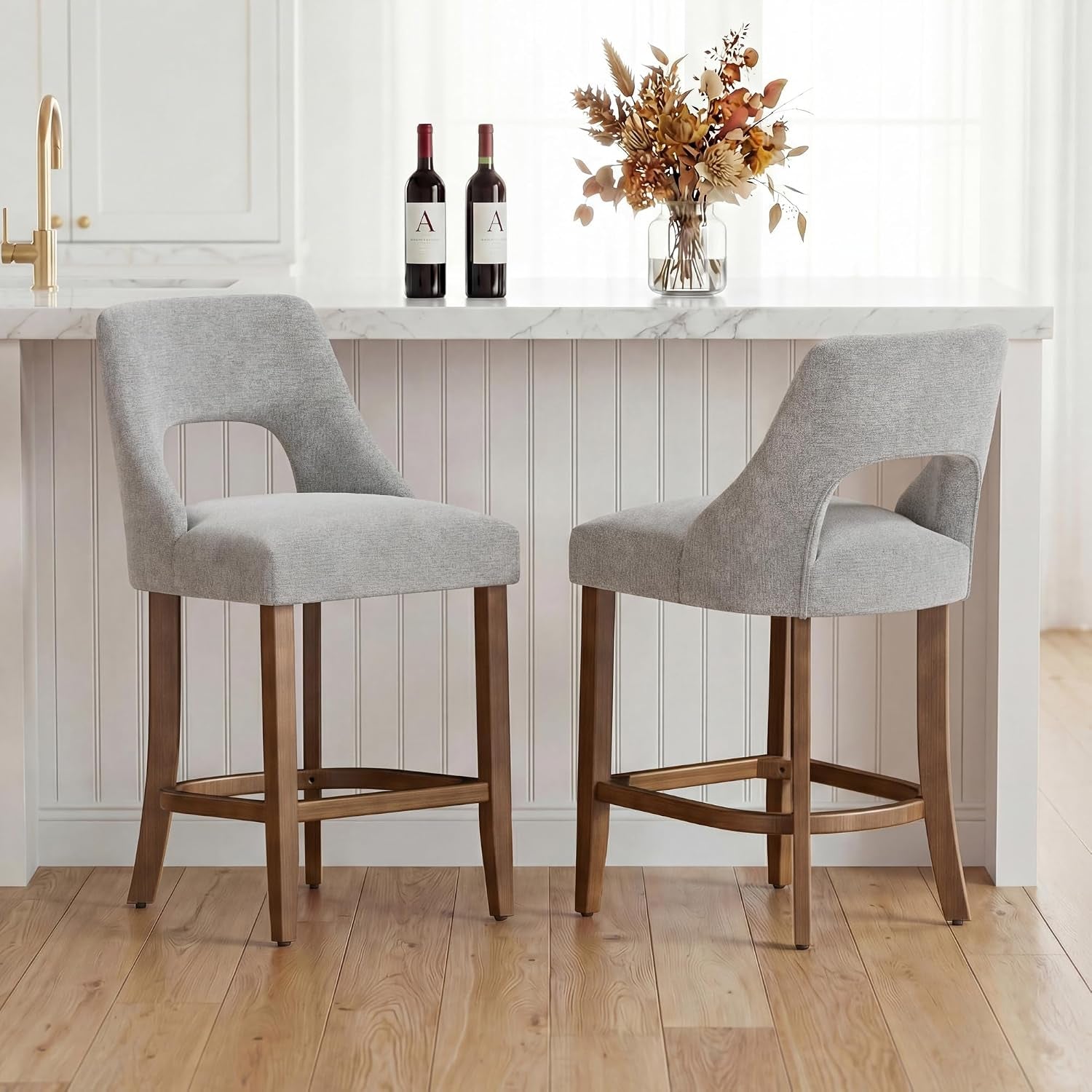 Two light gray upholstered counter stools with wood legs placed in front of a white island