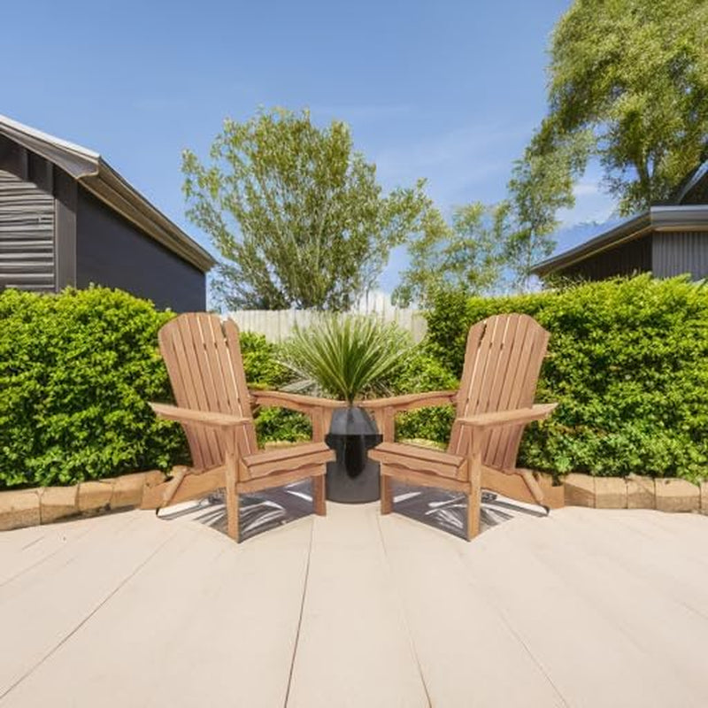 Two natural finish Adirondack chairs placed on a patio deck with green shrubs and a potted plant in the center
