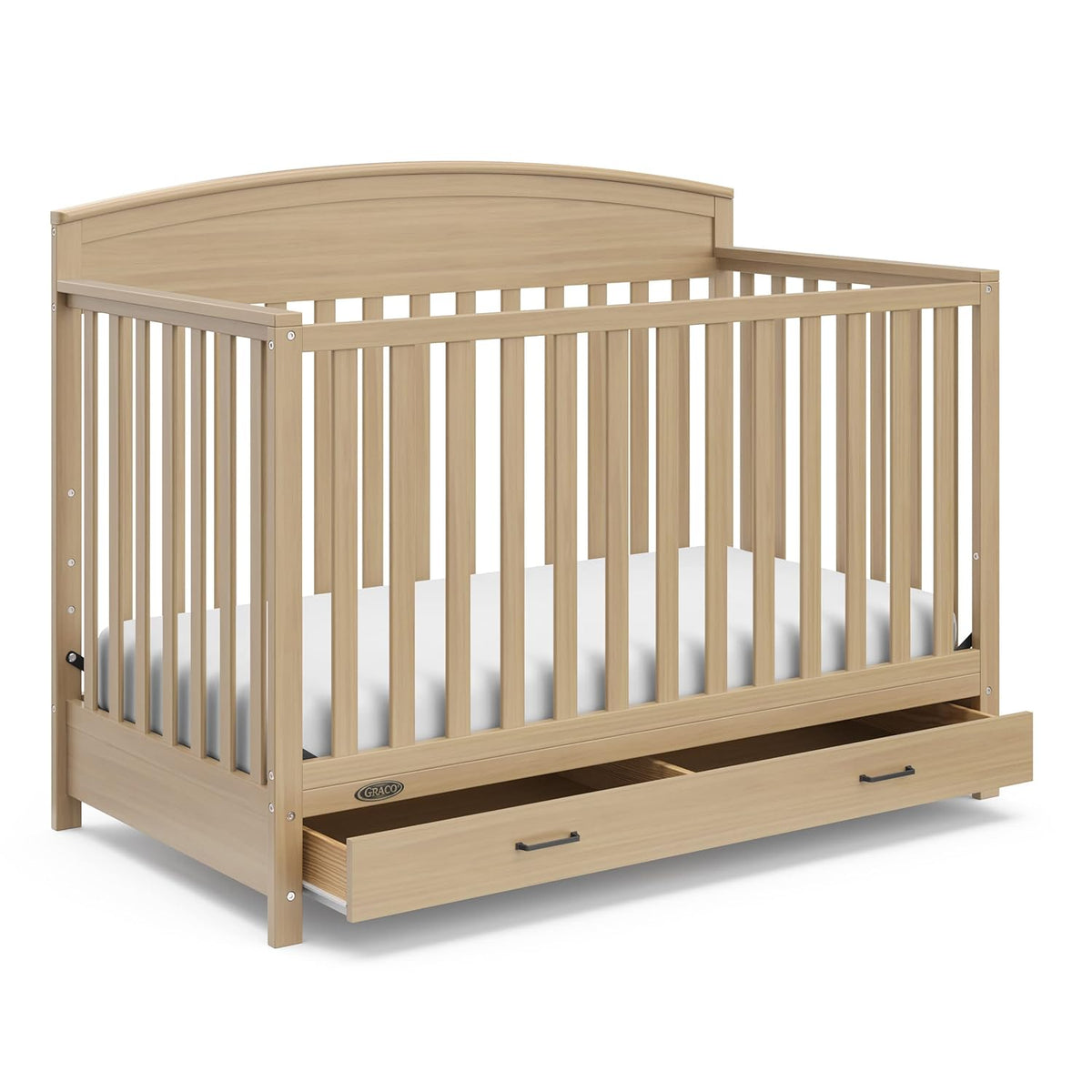 Light natural wood convertible crib with arched headboard, slatted sides, mattress and open under-drawer.
