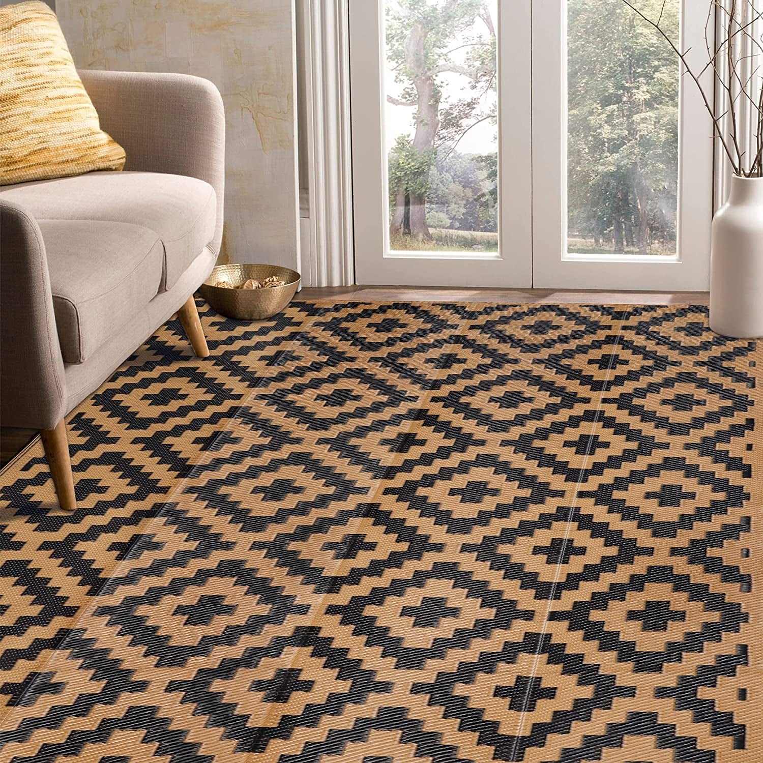 Interior entryway with sofa leg and tall vase, showing a tan-and-black patterned outdoor rug across the floor.