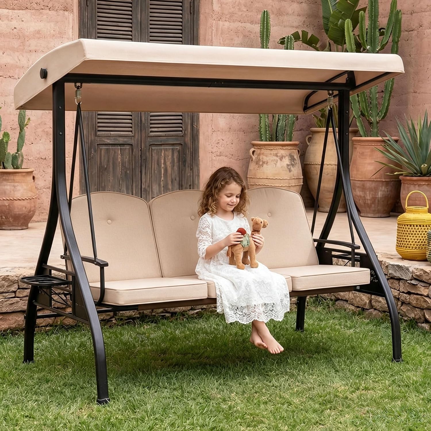 Three-seat outdoor swing with beige canopy and cushions; child in white dress sits on the seat.