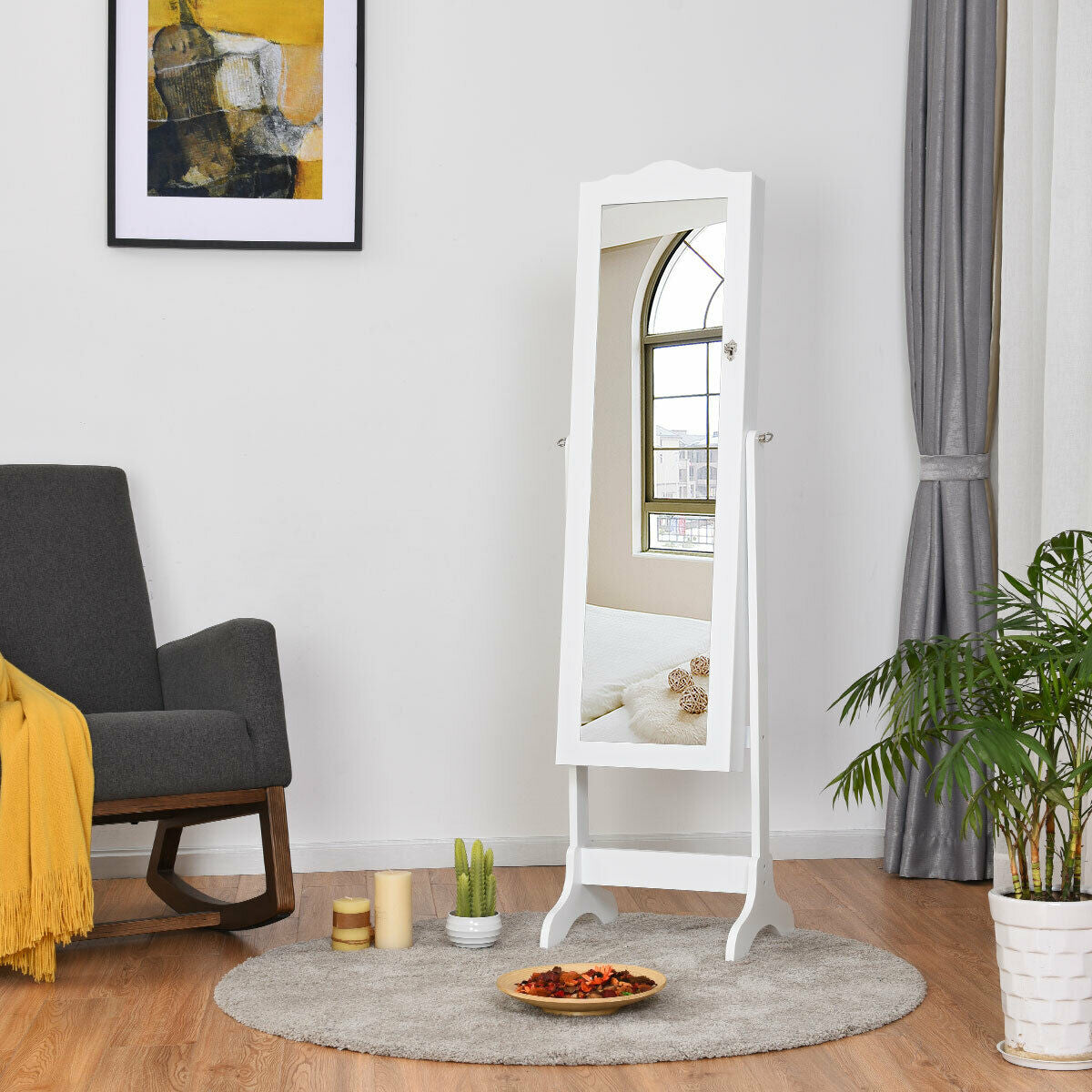 White full-length mirror jewelry armoire standing on a round rug beside a chair and curtains.
