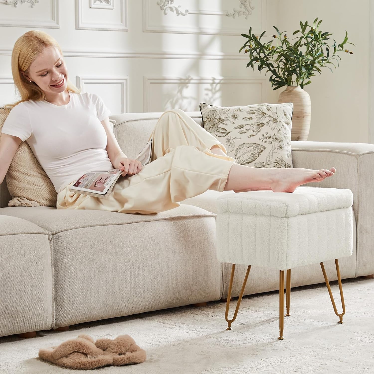 Living room scene with a woman lounging and a white faux-fur ottoman used as a footrest beside the sofa
