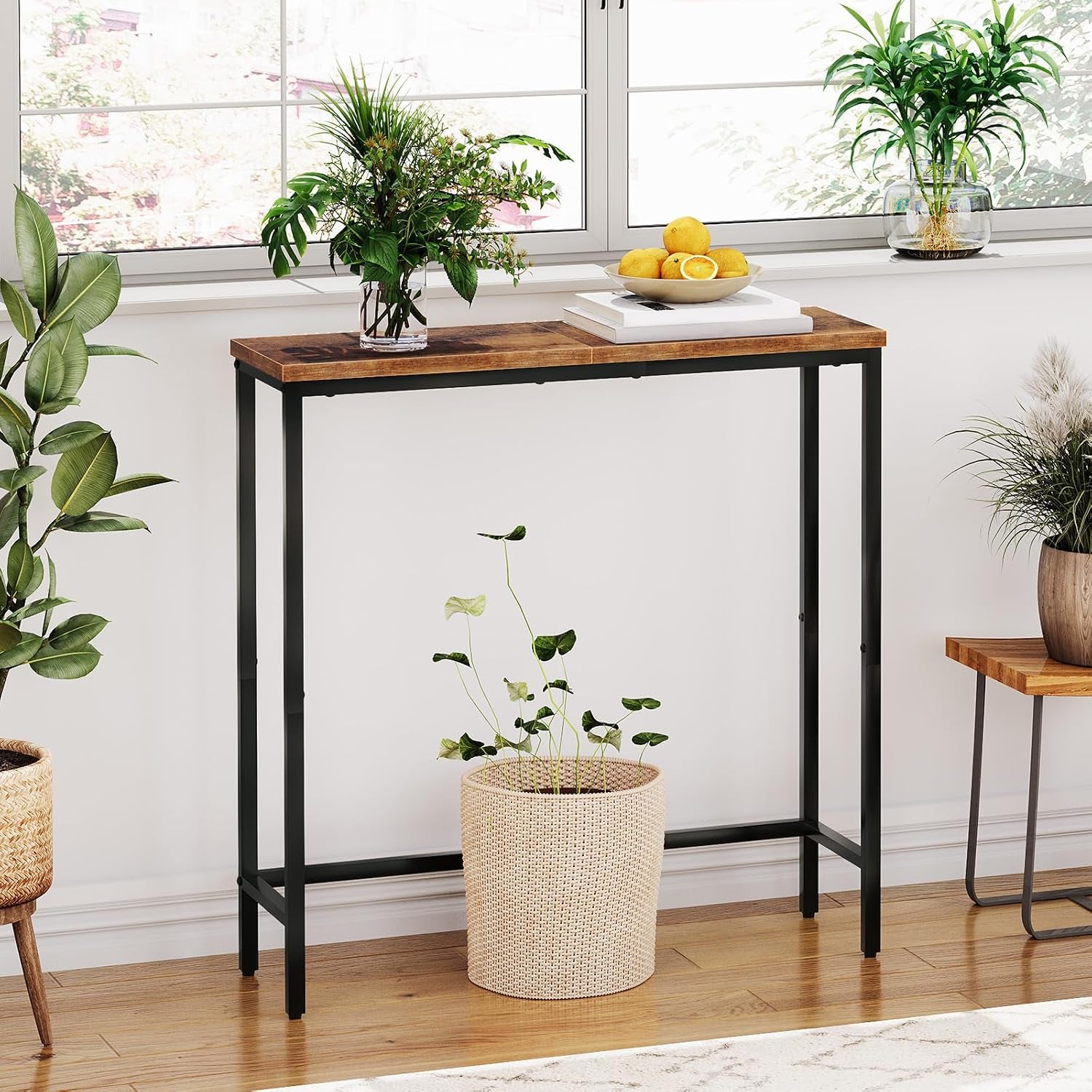 Single narrow console table with rustic wood top and black metal frame placed by a bright window with plants and a fruit