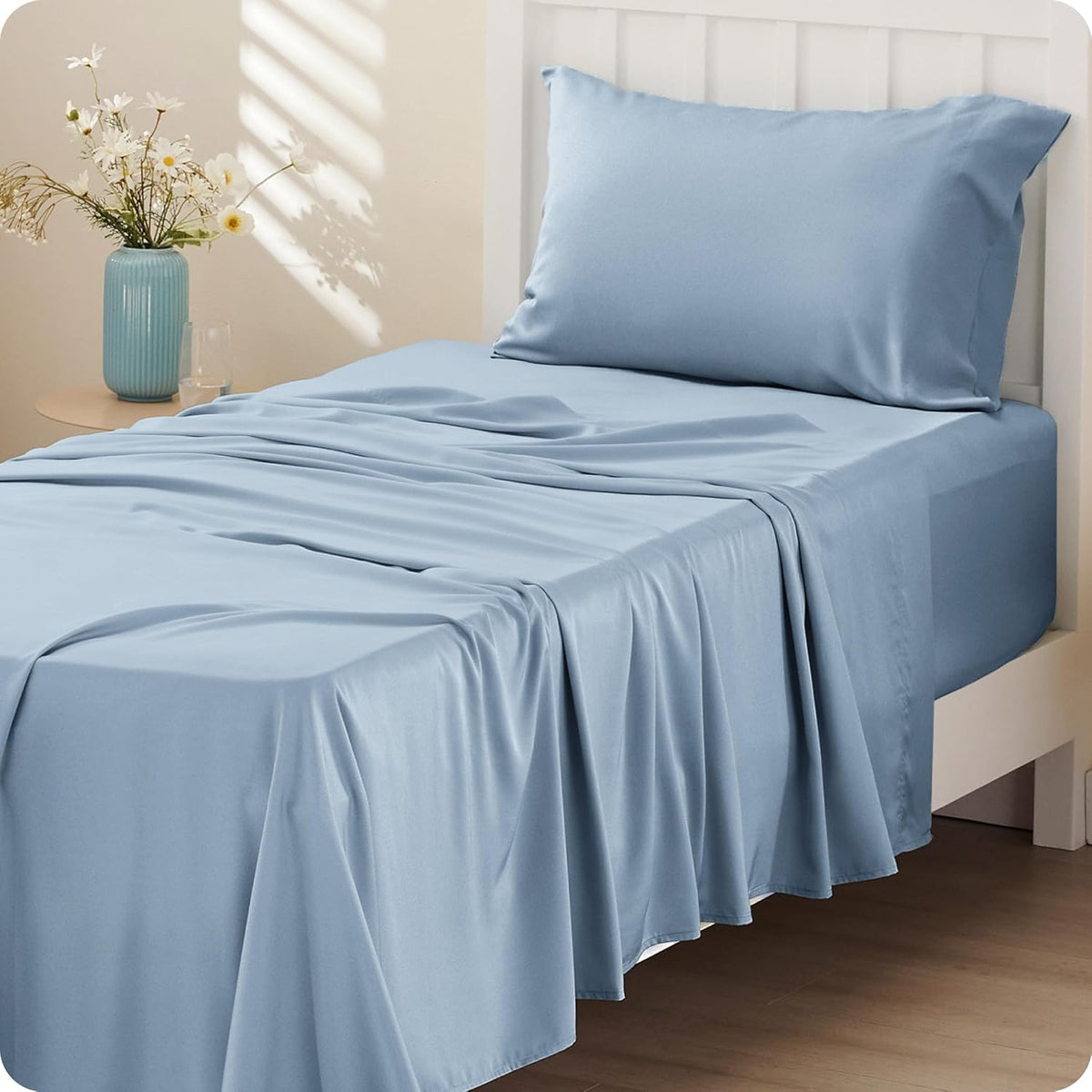 Close-up of a bed with light blue silky sheets and a matching pillow against a white headboard.