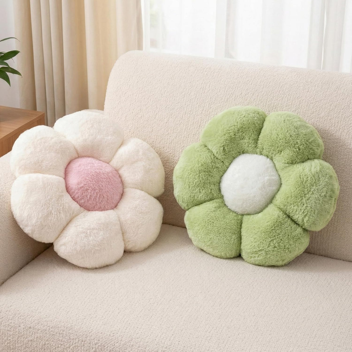Two plush flower pillows—one cream with pink center and one light green with white center—on a cream sofa.