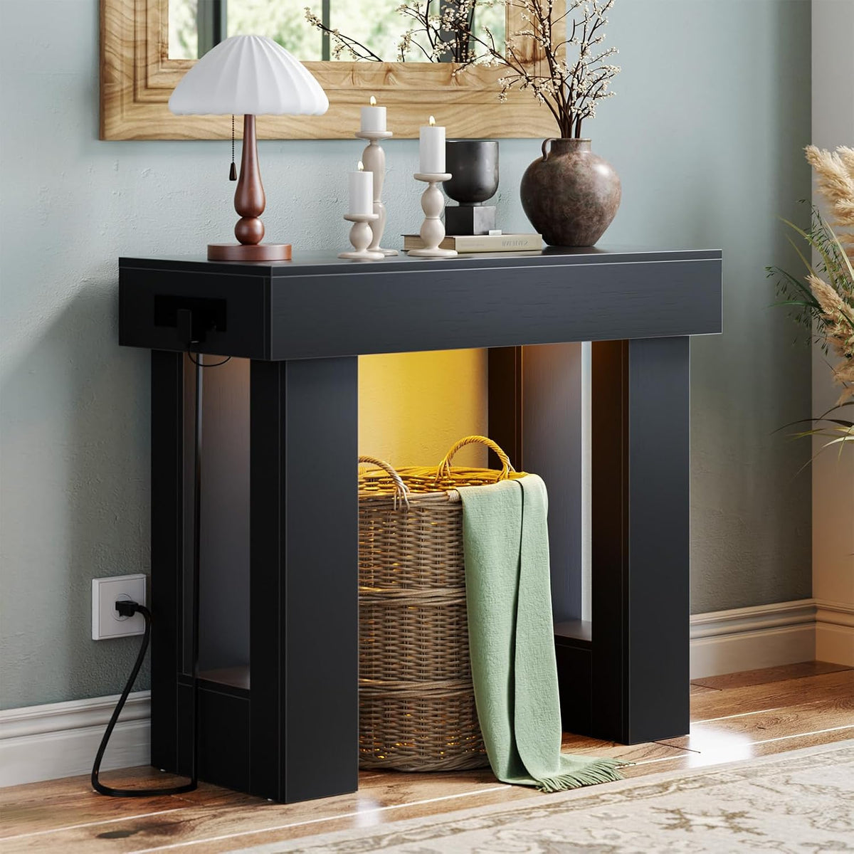 Angled close detail of a black console table corner with lamp on top and the power cord plugged into wall