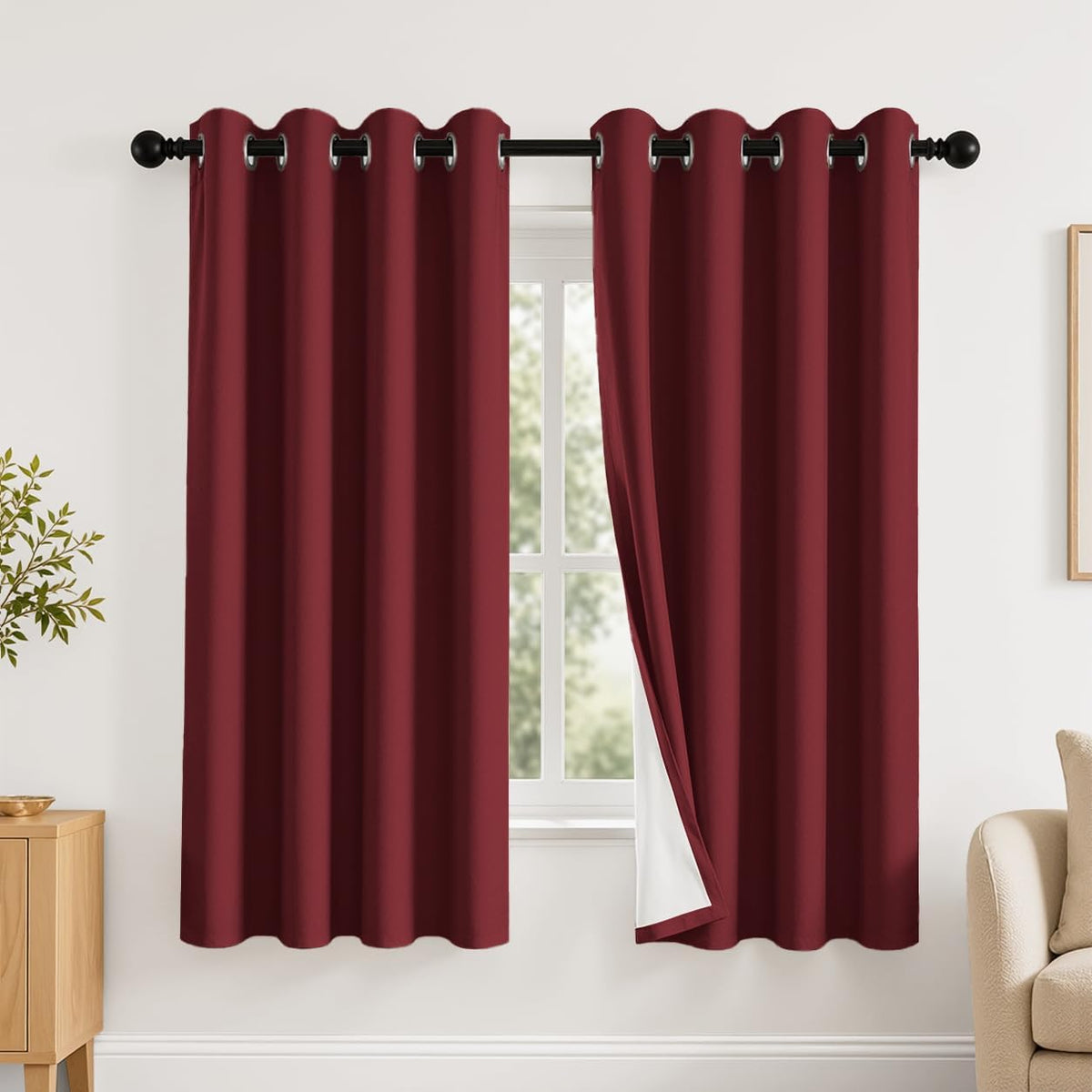 Window with two deep red grommet curtains on a black rod, one panel folded back revealing white backing.