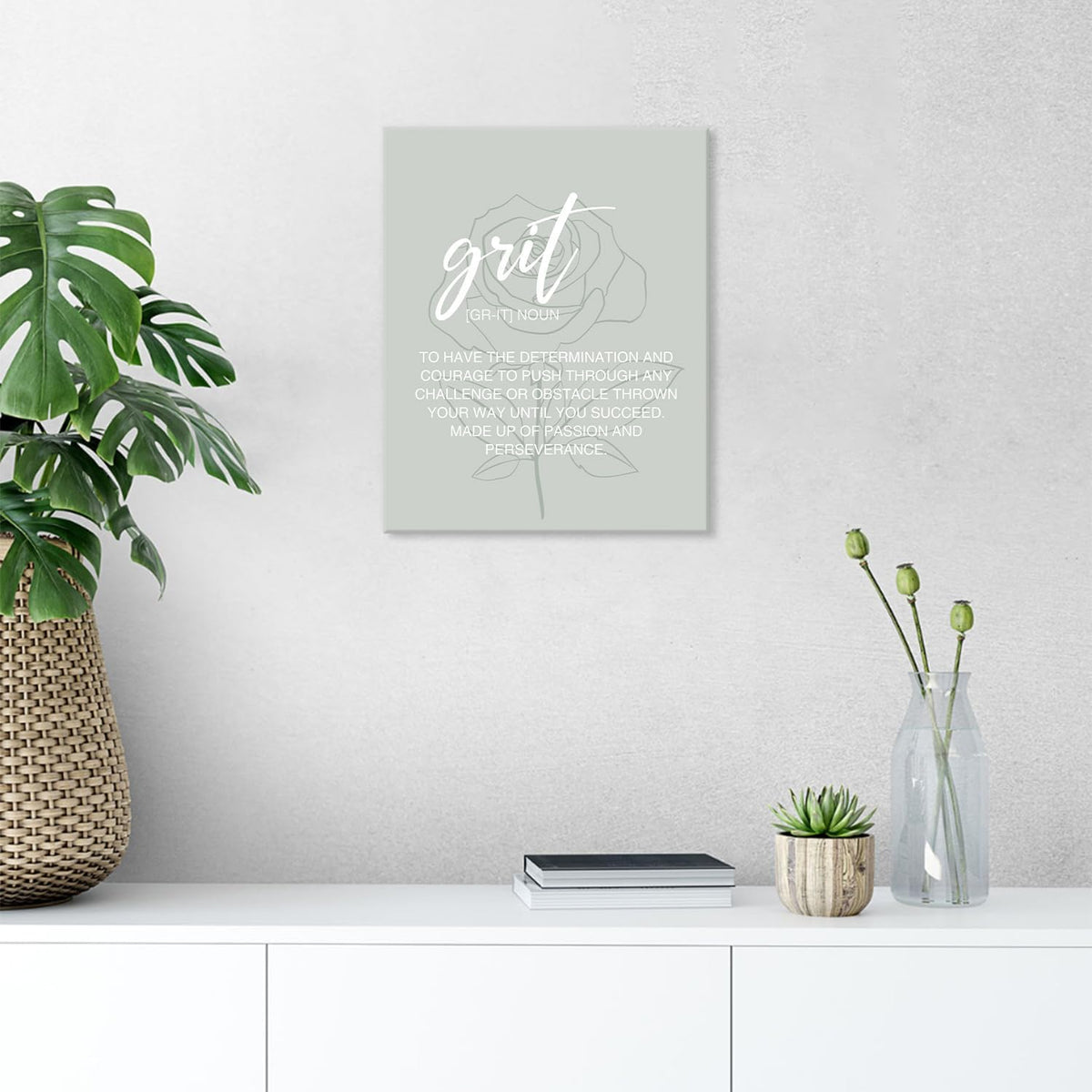 Single sage-green canvas print with 'grit' typography hung above a white console next to potted plants and vases