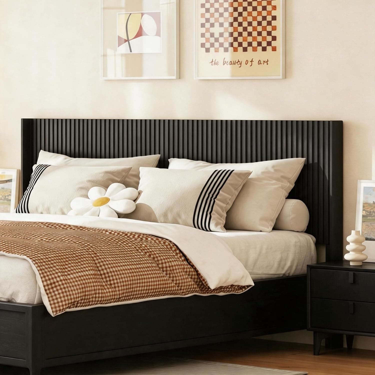 Angled view of a black fluted headboard on a bed with cream pillows and a gingham throw.