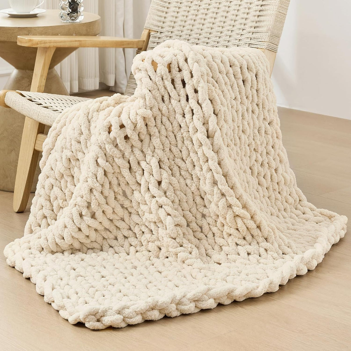 Cream chunky knit throw arranged over a woven wood chair with a side table and lamp nearby.