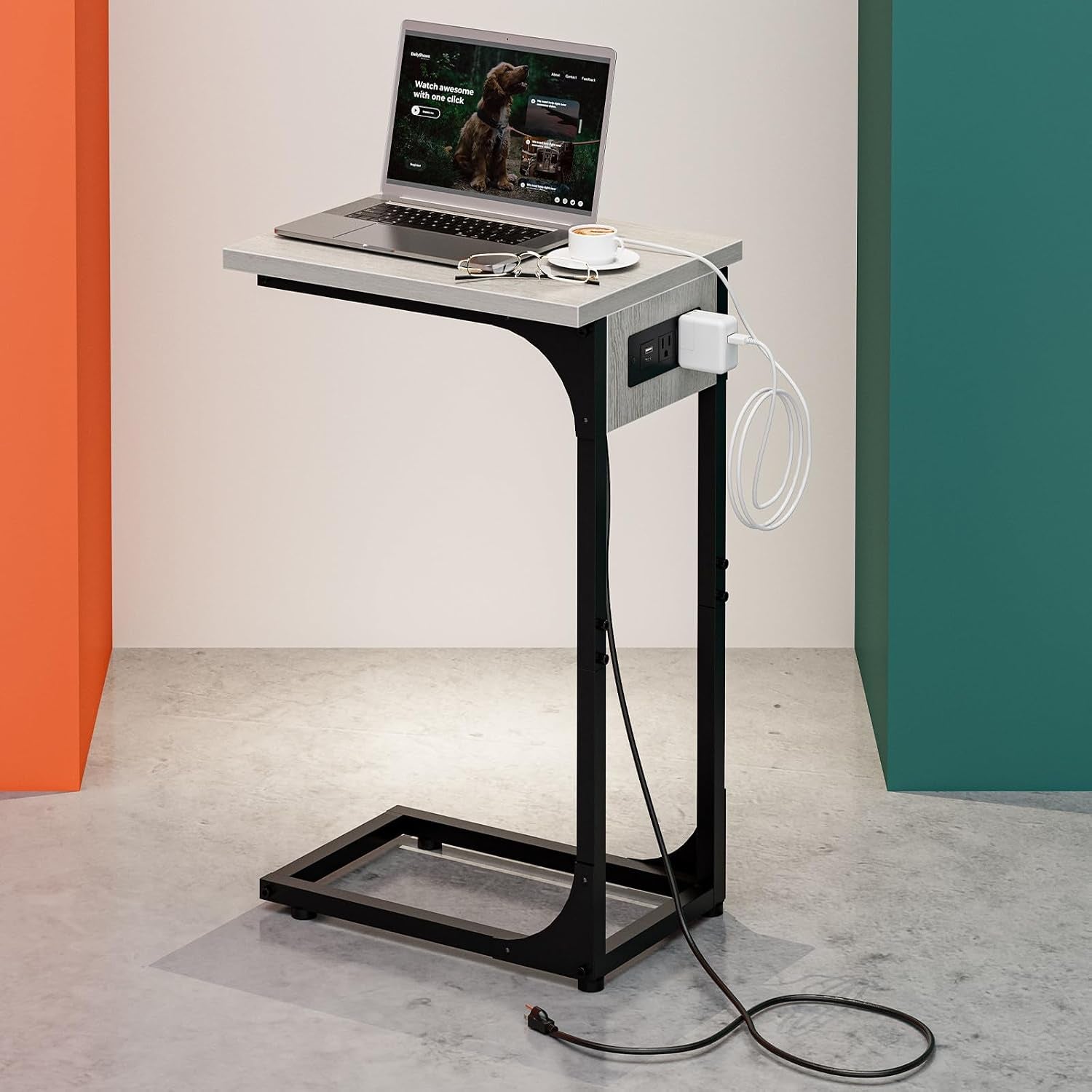 Single C-shaped end table with light gray top and black steel frame, laptop on top and power outlet visible on the side.