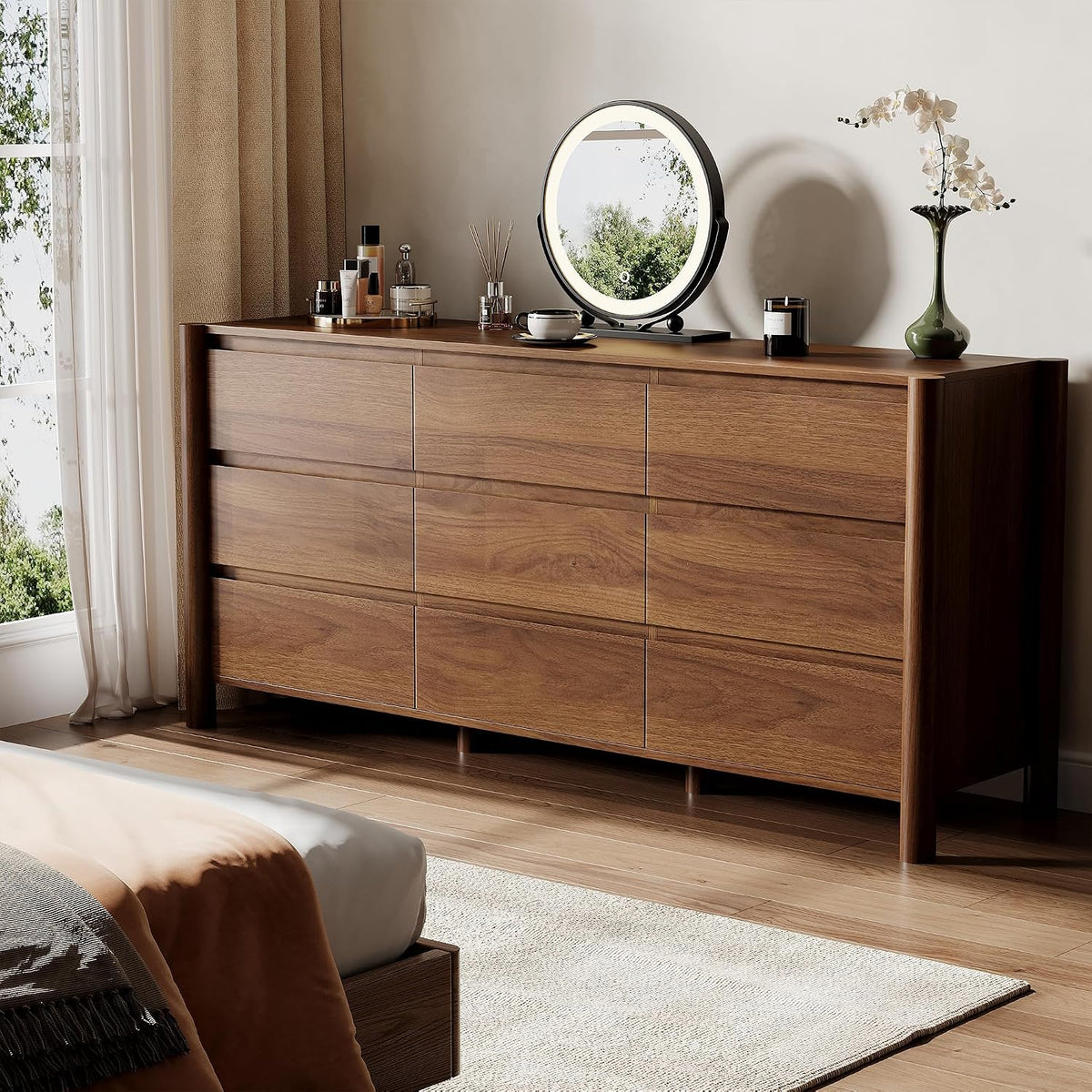 Angled close view of a wide walnut dresser topped with mirror, vase and decor in a sunlit bedroom.