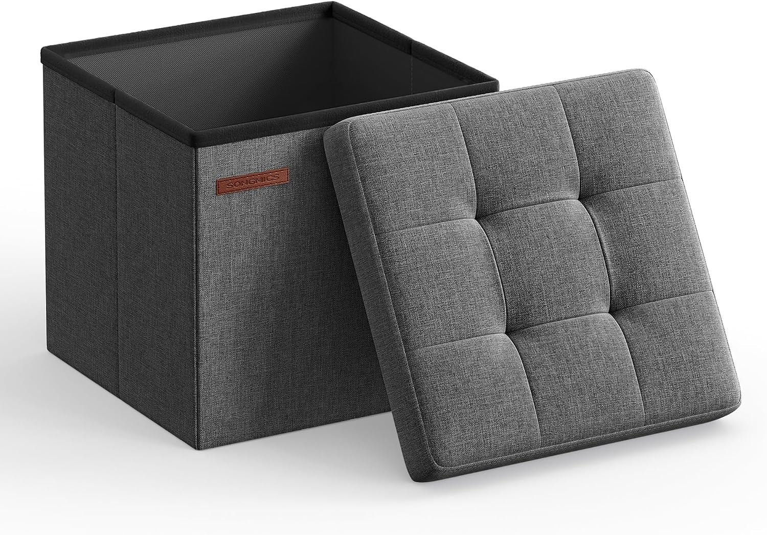 Angled view of a gray fabric storage ottoman with the lid removed; tufted lid leans against the box showing the interior.