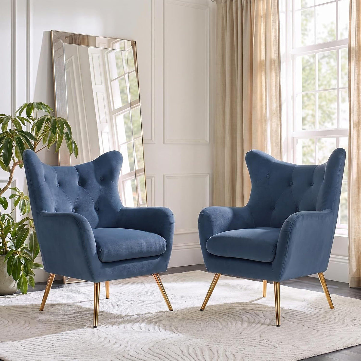 Pair of blue velvet wingback chairs facing forward in a sunlit corner with a leaning mirror