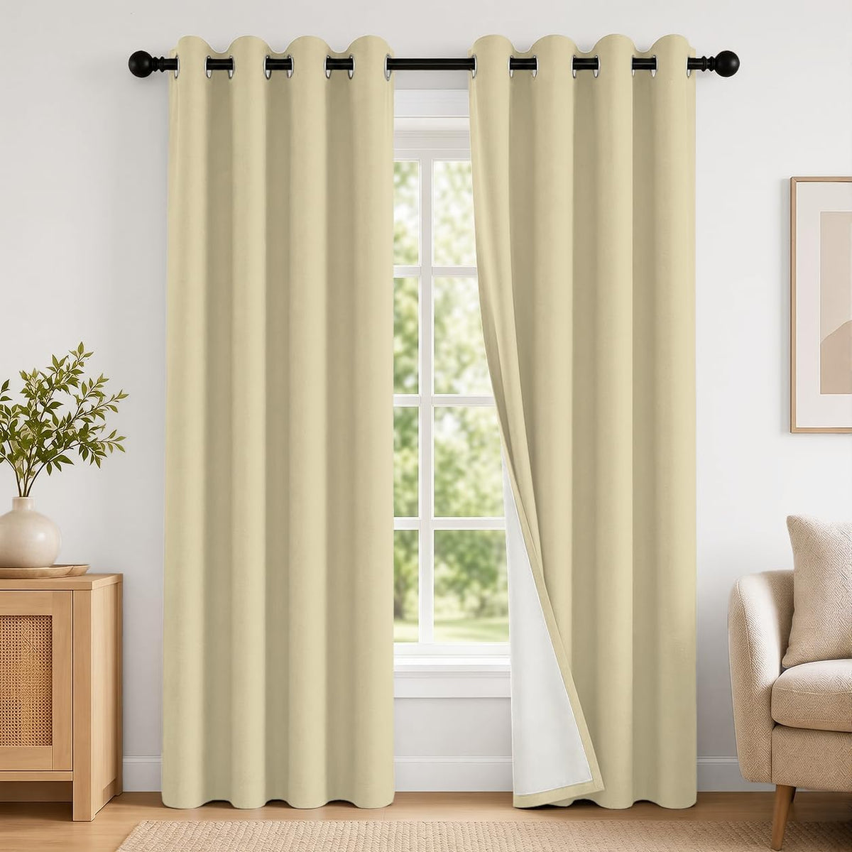 Light beige grommet-top blackout curtains parted to show white backing and a window with greenery outside.