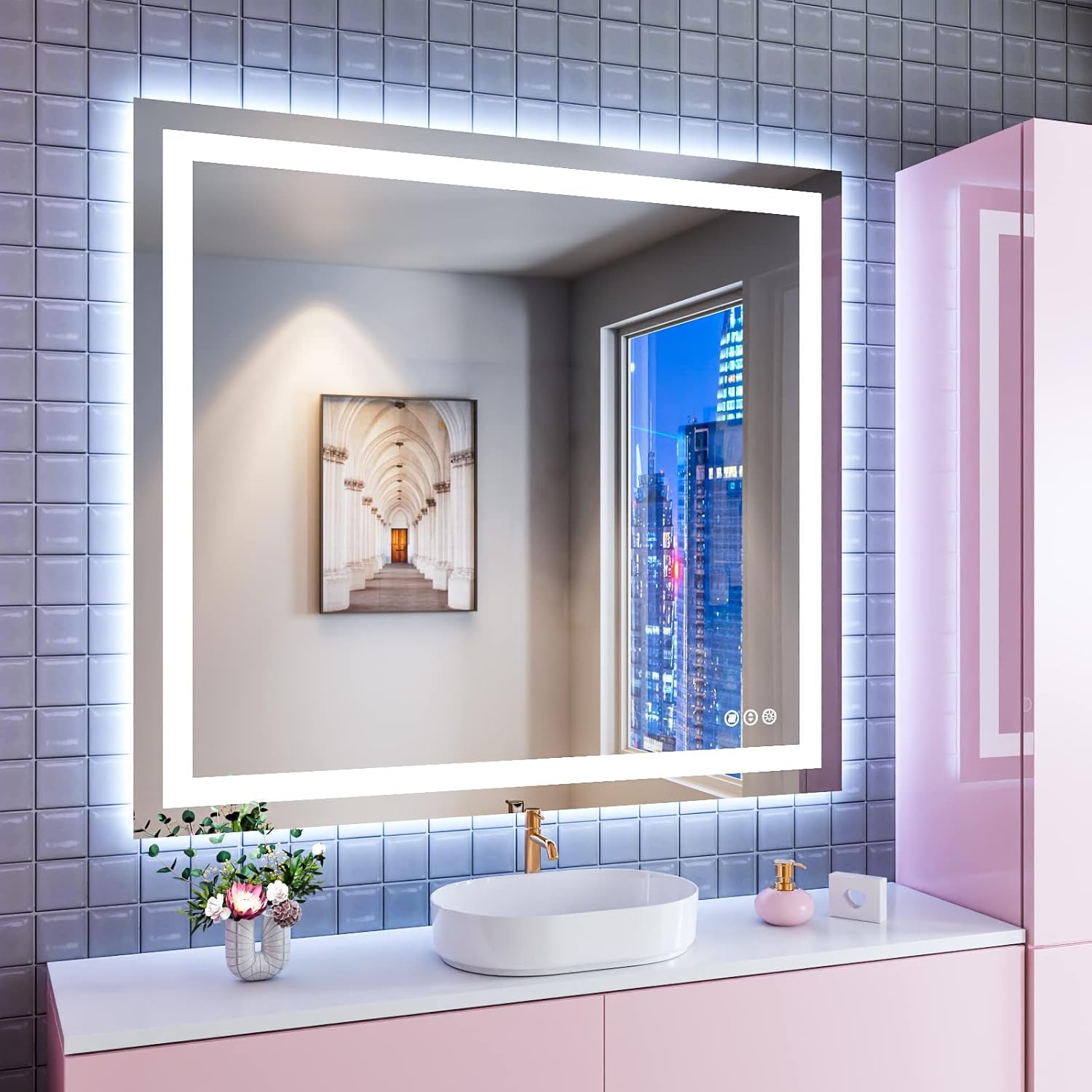 Glowing LED mirror above a pink vanity with an oval vessel sink, tiled wall and a framed picture reflected in the glass.