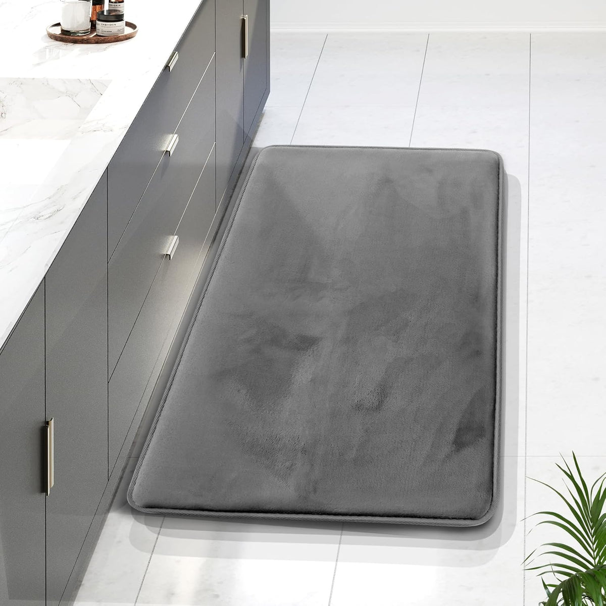 Long gray rectangular memory-foam runner beside a dark vanity, shown from above with a plant frond at the edge.