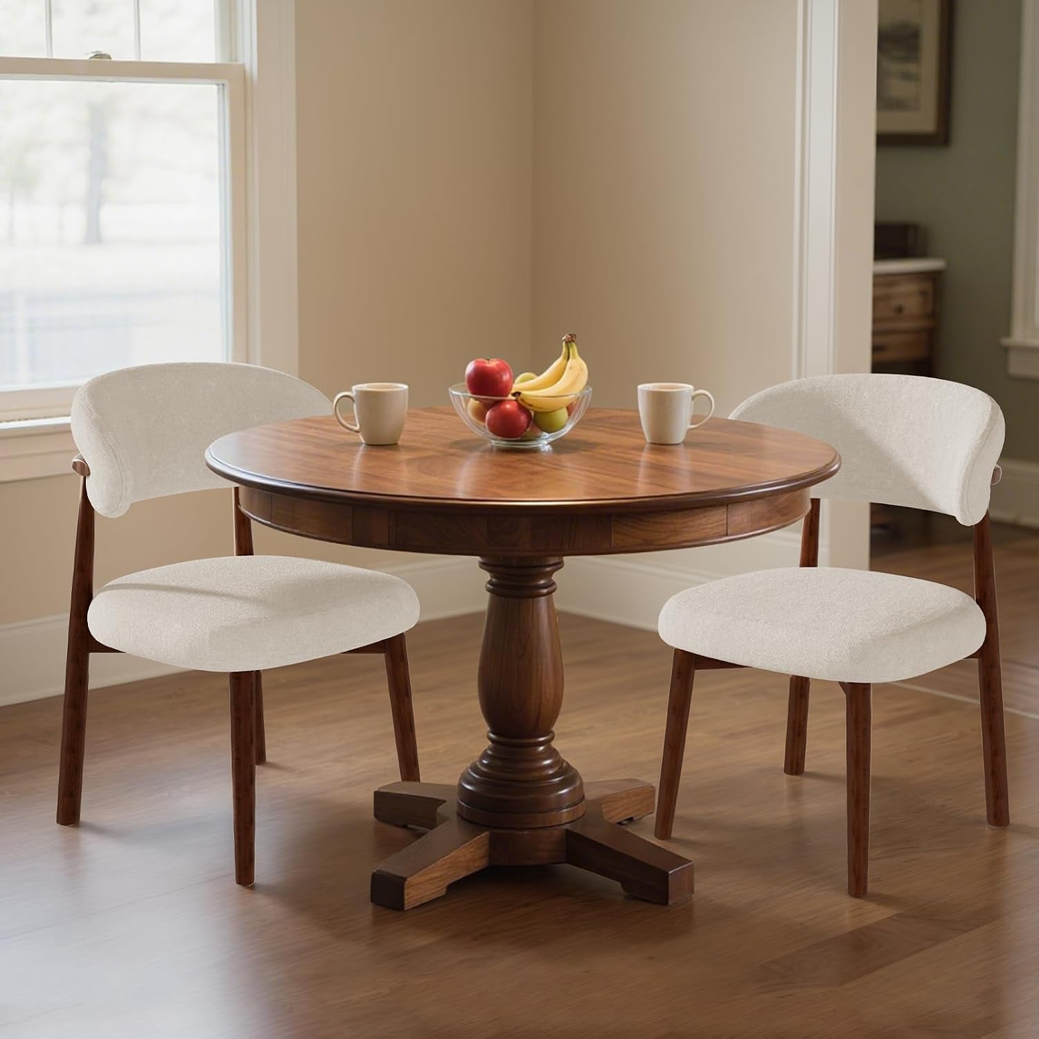 Two ivory upholstered curved-back chairs with brown frames at a round dining table.