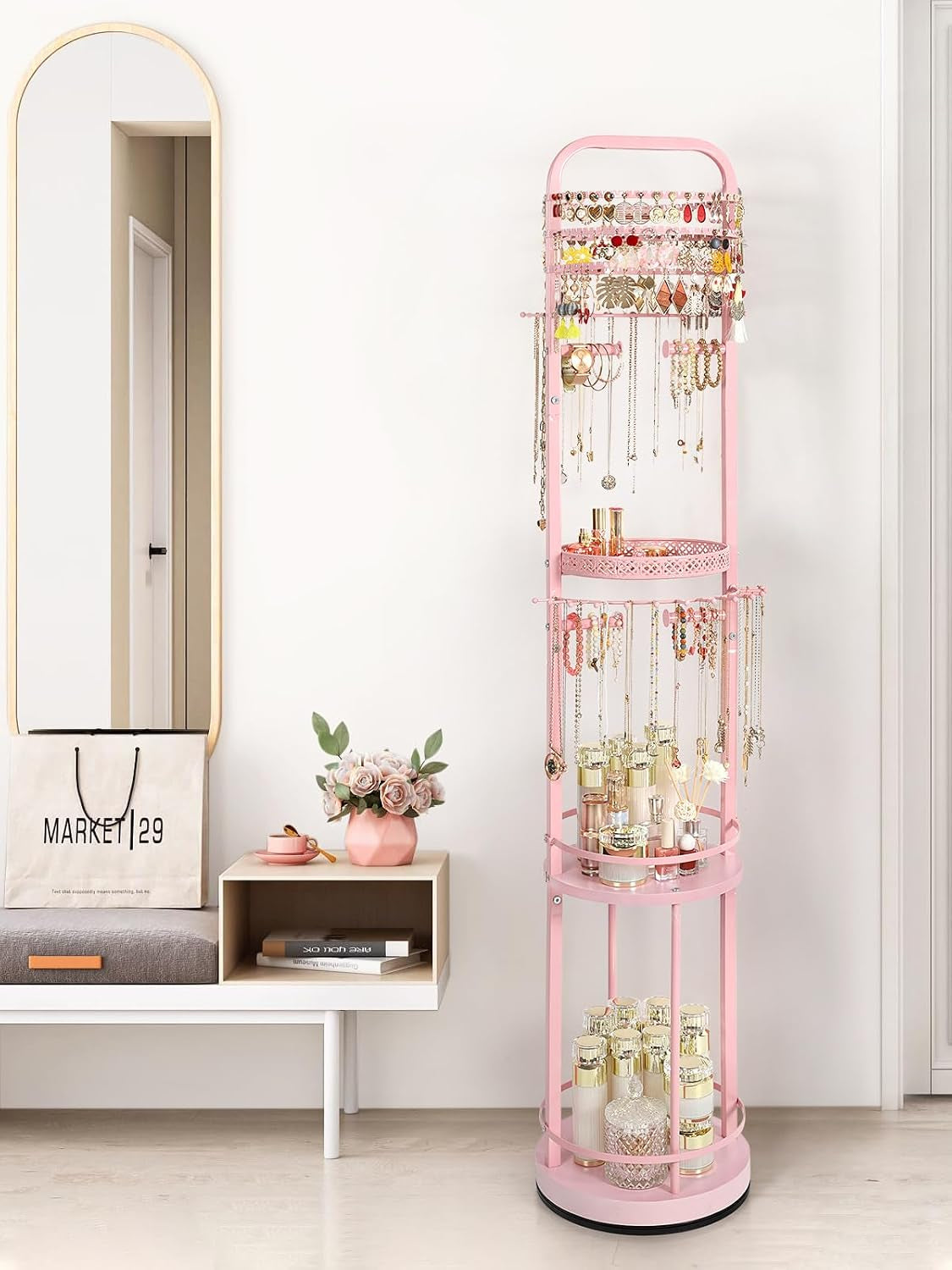 Slim pink jewelry stand with hanging chains and displayed jars placed by an entry bench and mirror.