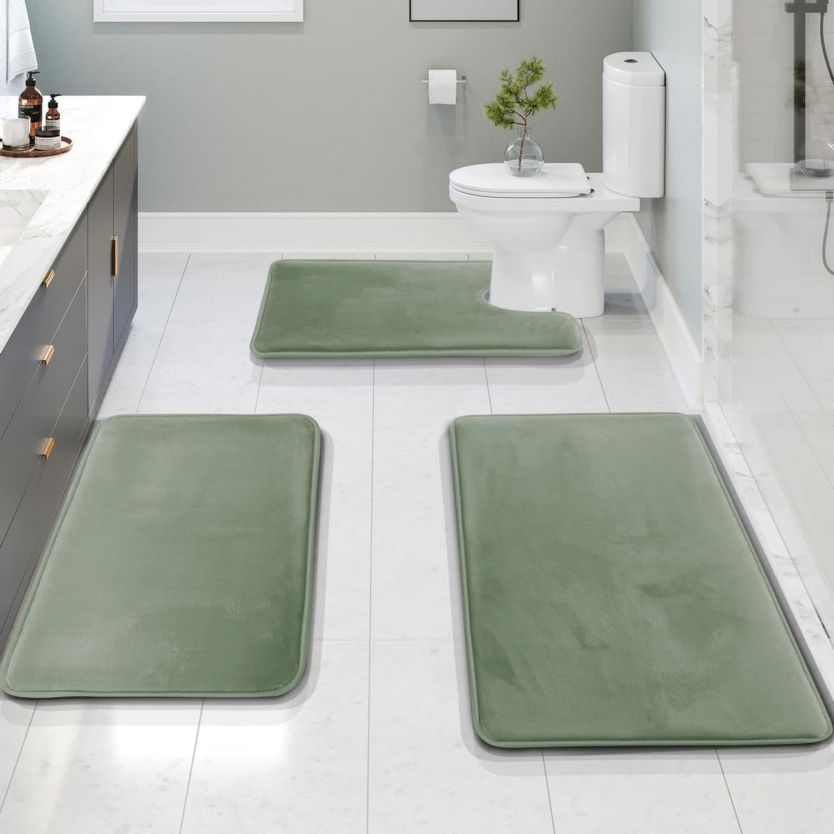 Perspective view of three sage-green bath mats arranged on white tile, showing the U-shaped piece positioned around the