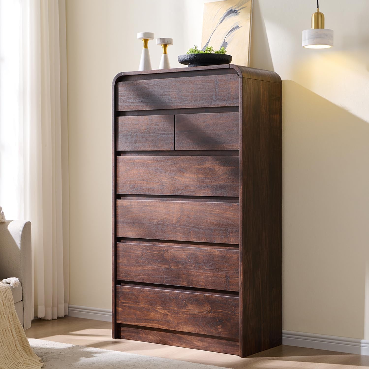Tall dark-wood chest photographed slightly from the right with pendant light and decor on top.