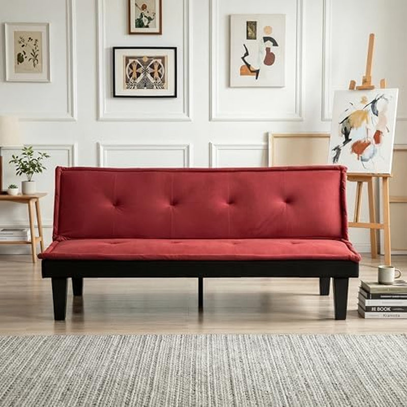 Red futon sofa seen straight on against paneled wall with artwork and easel, black wooden legs visible.