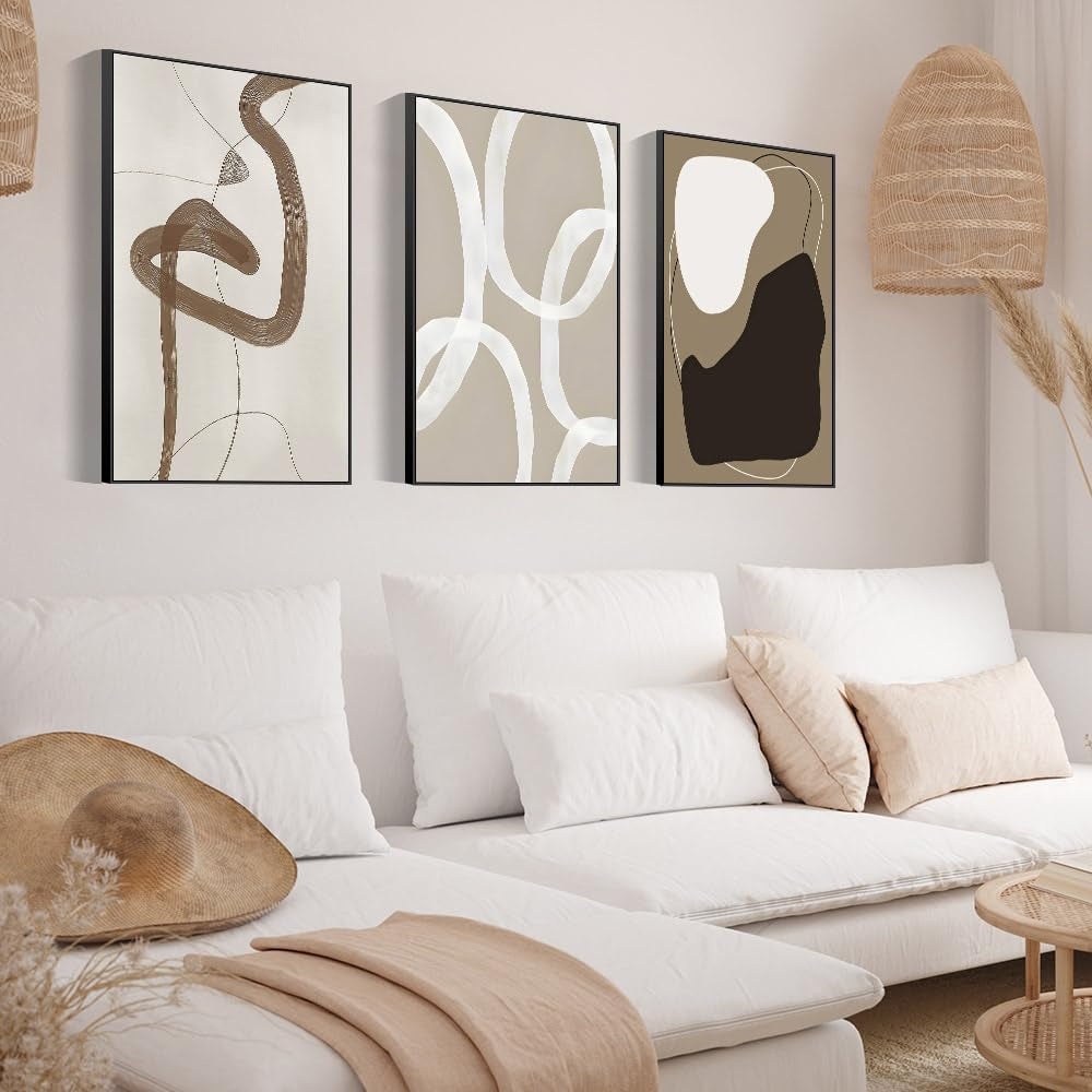 Set of three beige-and-brown abstract framed canvases displayed above a white sofa in a neutral boho living room with woven