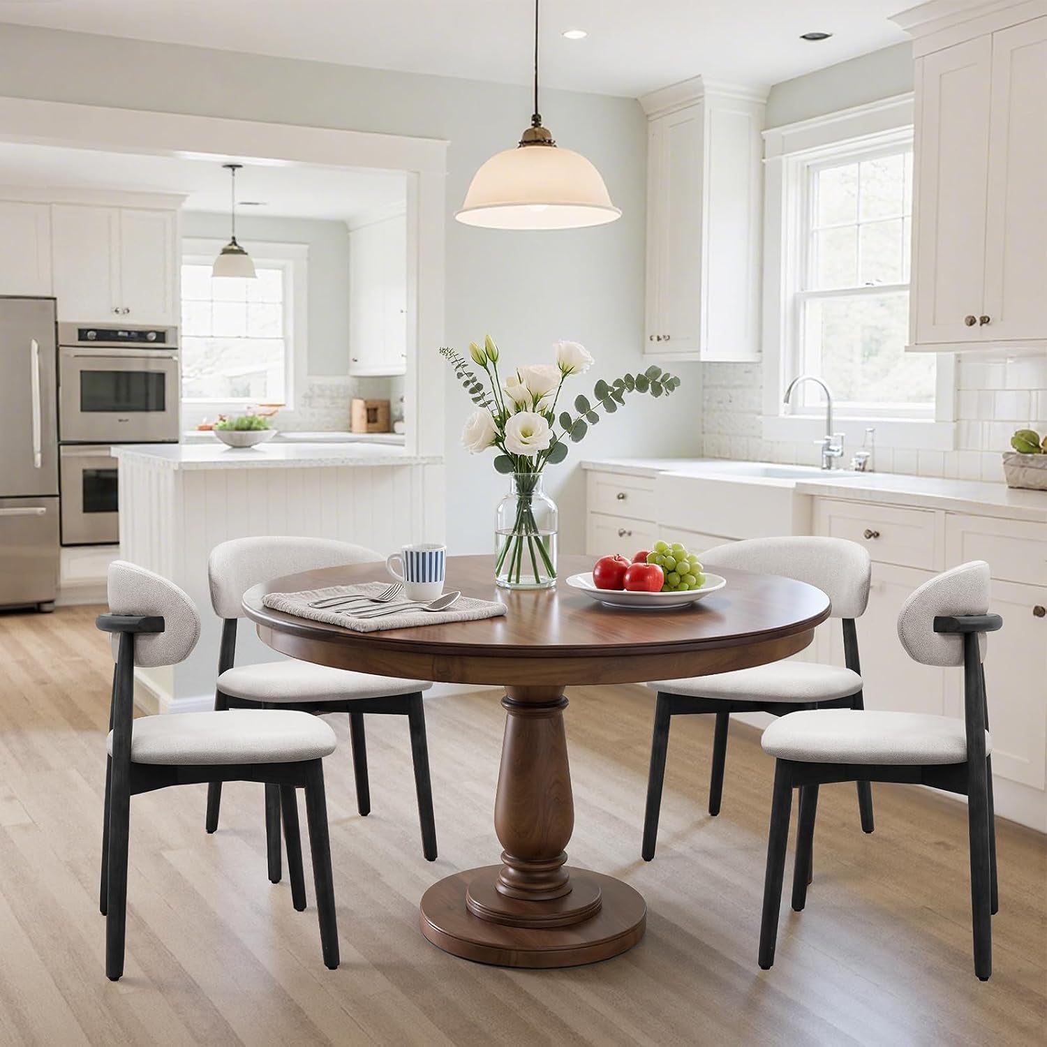 Four cream upholstered chairs with black frames surround a round wood table in a white kitchen.