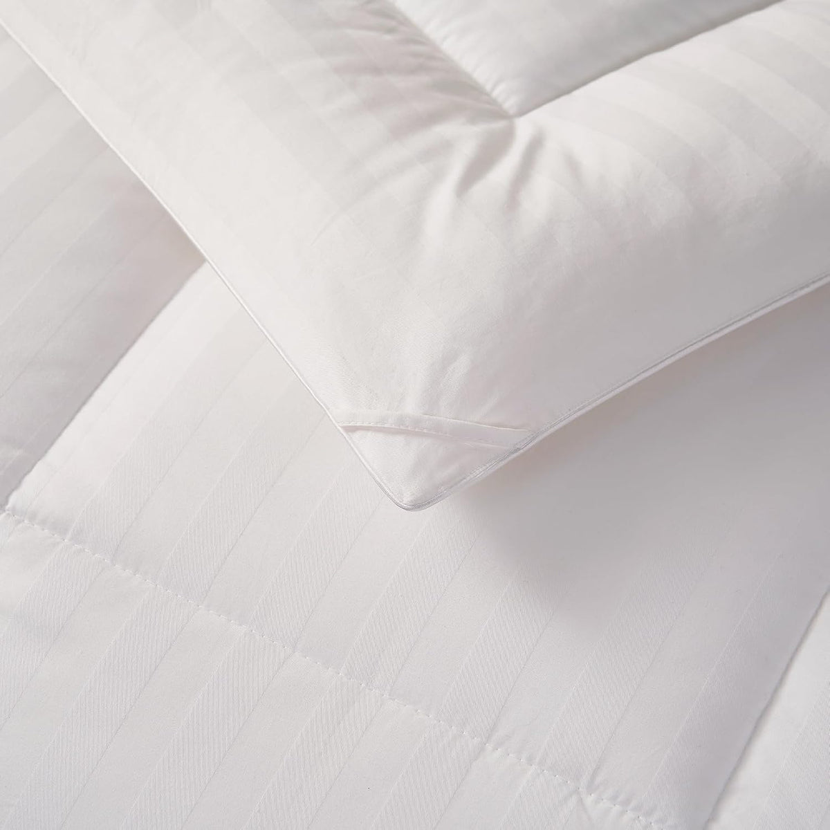 Angled close view of a pillow corner resting on a quilted striped comforter, showing piped edge and box stitching