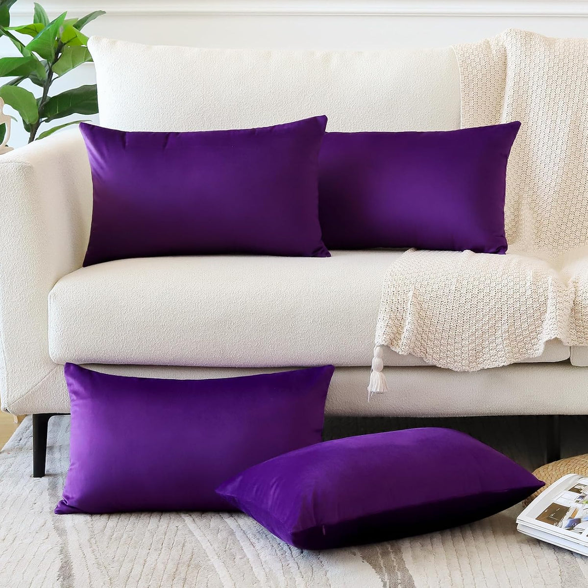 Two deep purple rectangular throw pillow covers on a cream sofa with matching purple pillows on the floor