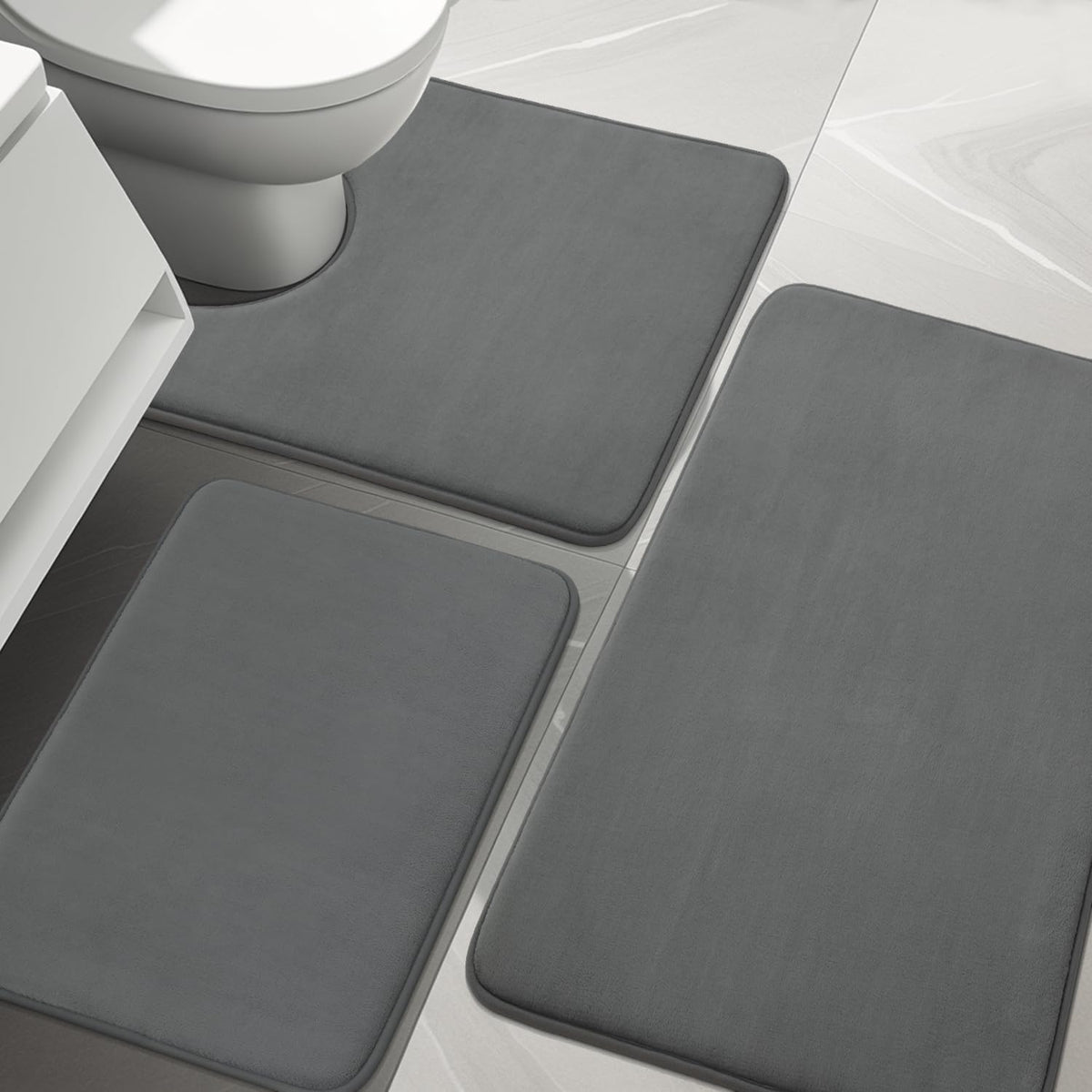 Close top-down view of three charcoal-gray rectangular bath rugs on light tile flooring.