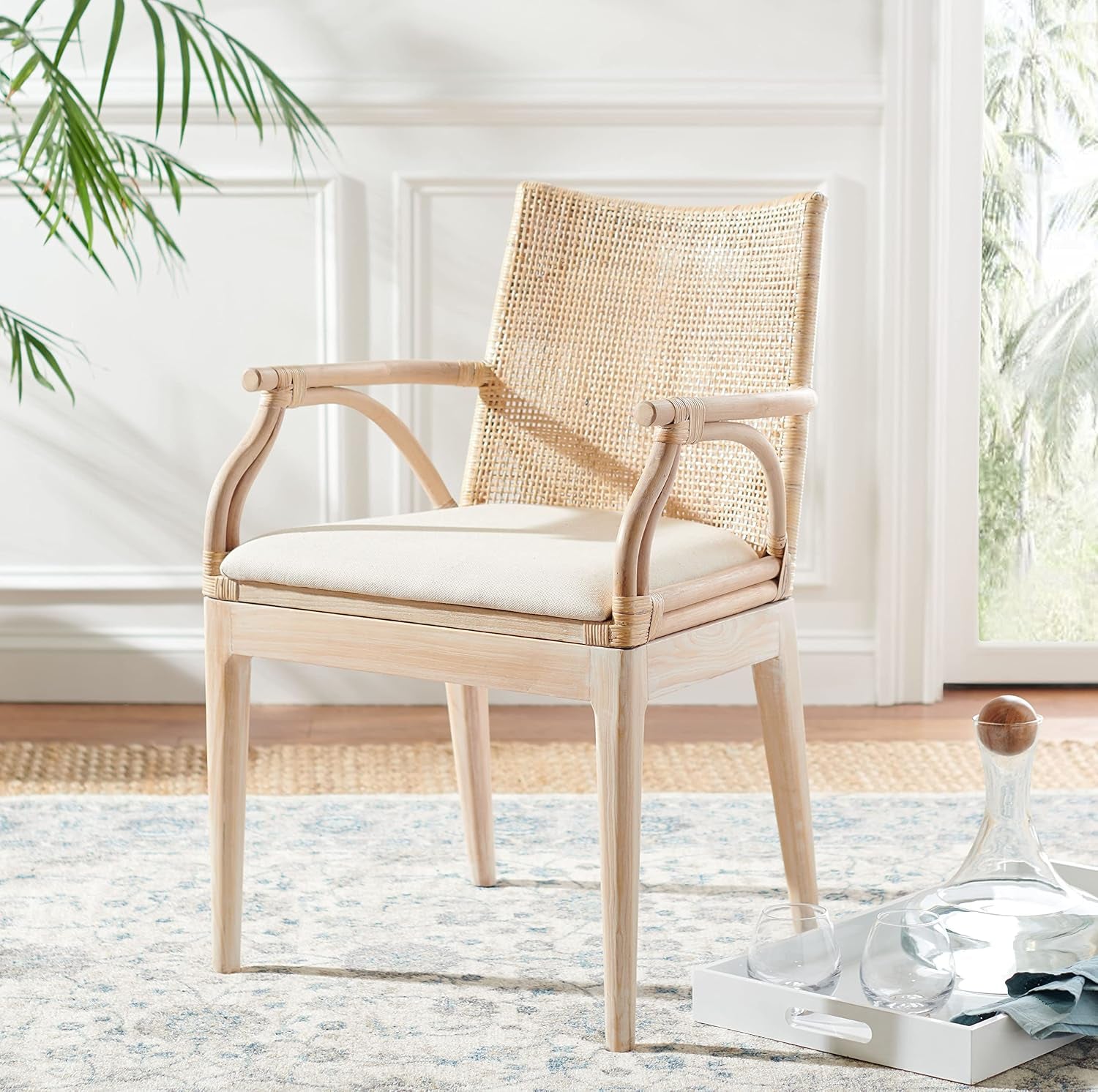 Full view of a rattan-back armchair with light wood frame and cream seat cushion in a bright room.