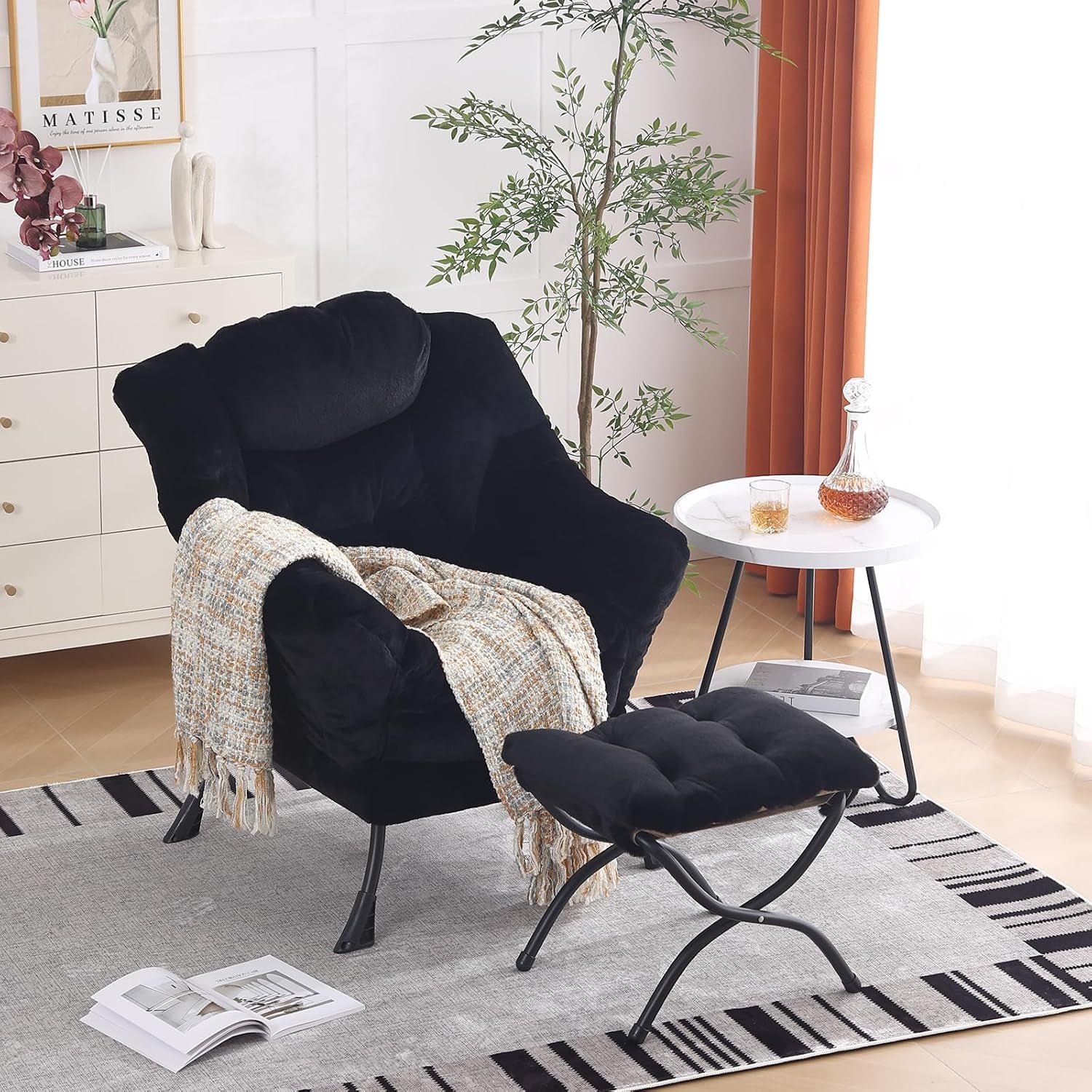 Black cushioned chair and ottoman in a bright living corner with side table, plant, and throw
