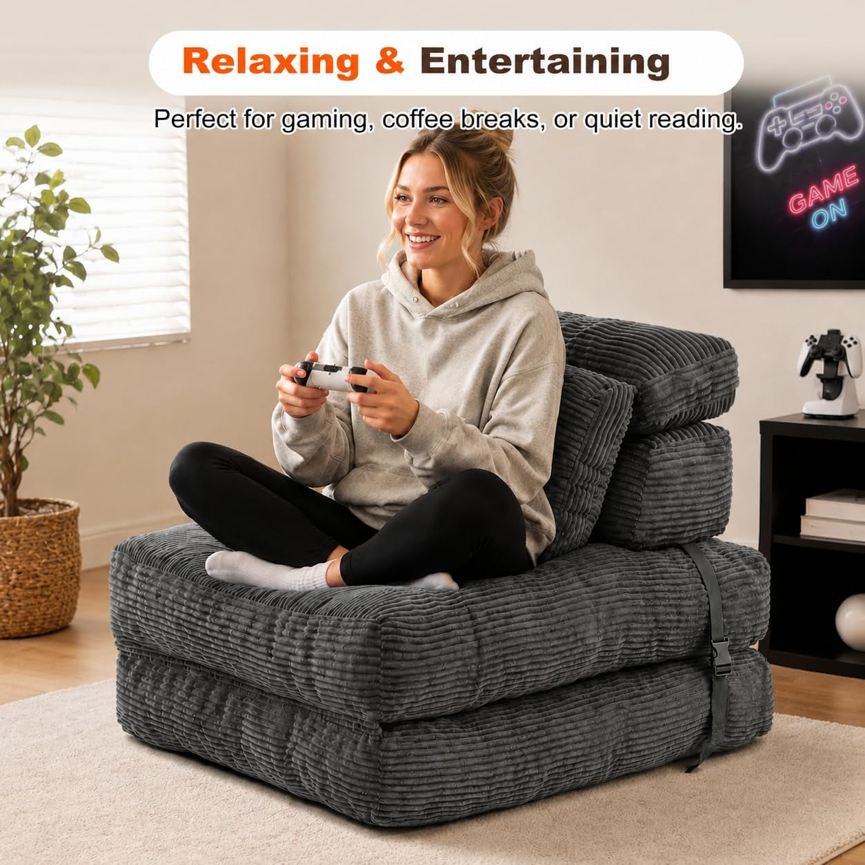 Person sitting cross-legged on a dark grey corduroy folding floor chair while playing a game controller.