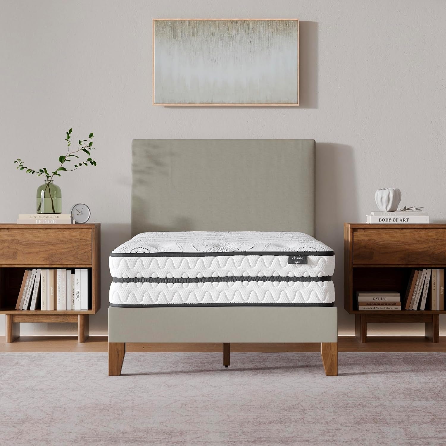 Front view of a white pillow-top mattress on a gray upholstered bedframe, flanked by wooden nightstands and wall art.