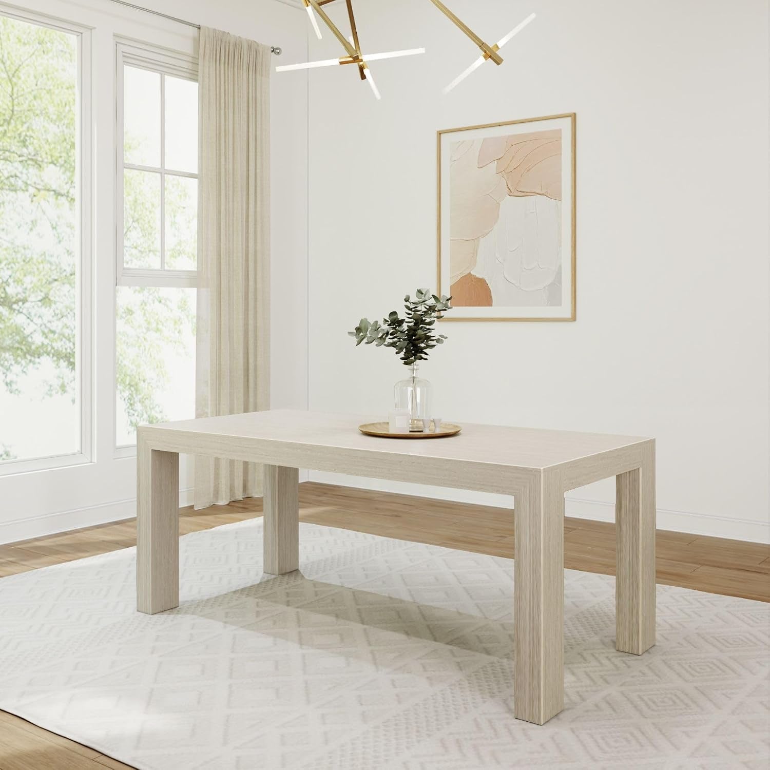 Light-colored rectangular pine dining table in a bright room on a patterned rug, vase centerpiece visible
