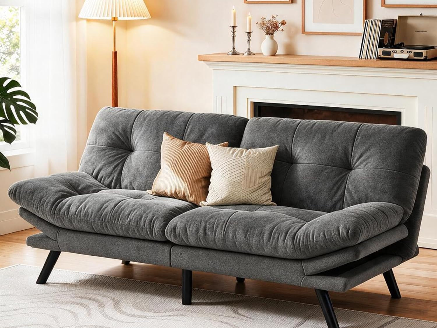 Medium gray convertible futon sofa with tufted cushions and two throw pillows in a bright living room