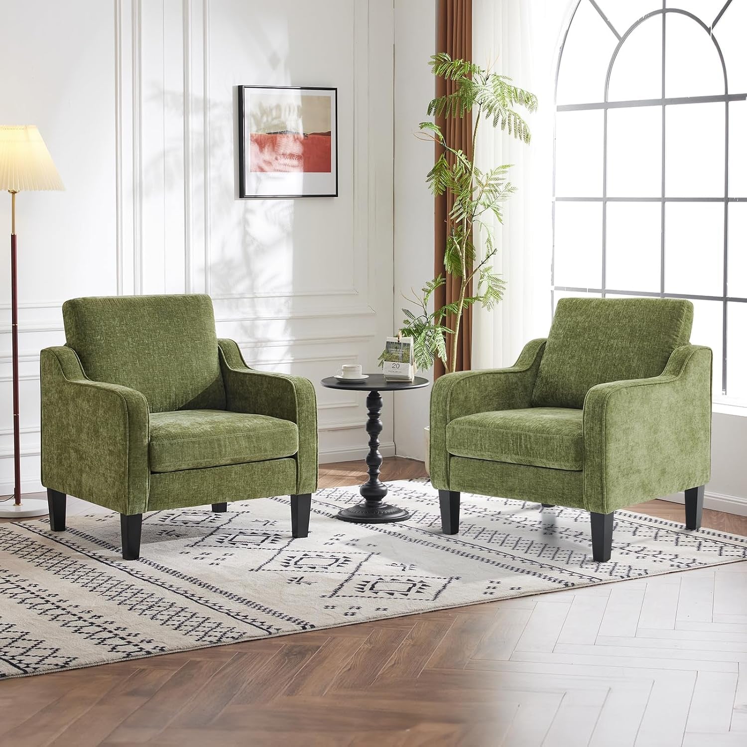 Pair of olive-green club chairs with tapered dark legs arranged on a patterned rug around a small pedestal table.