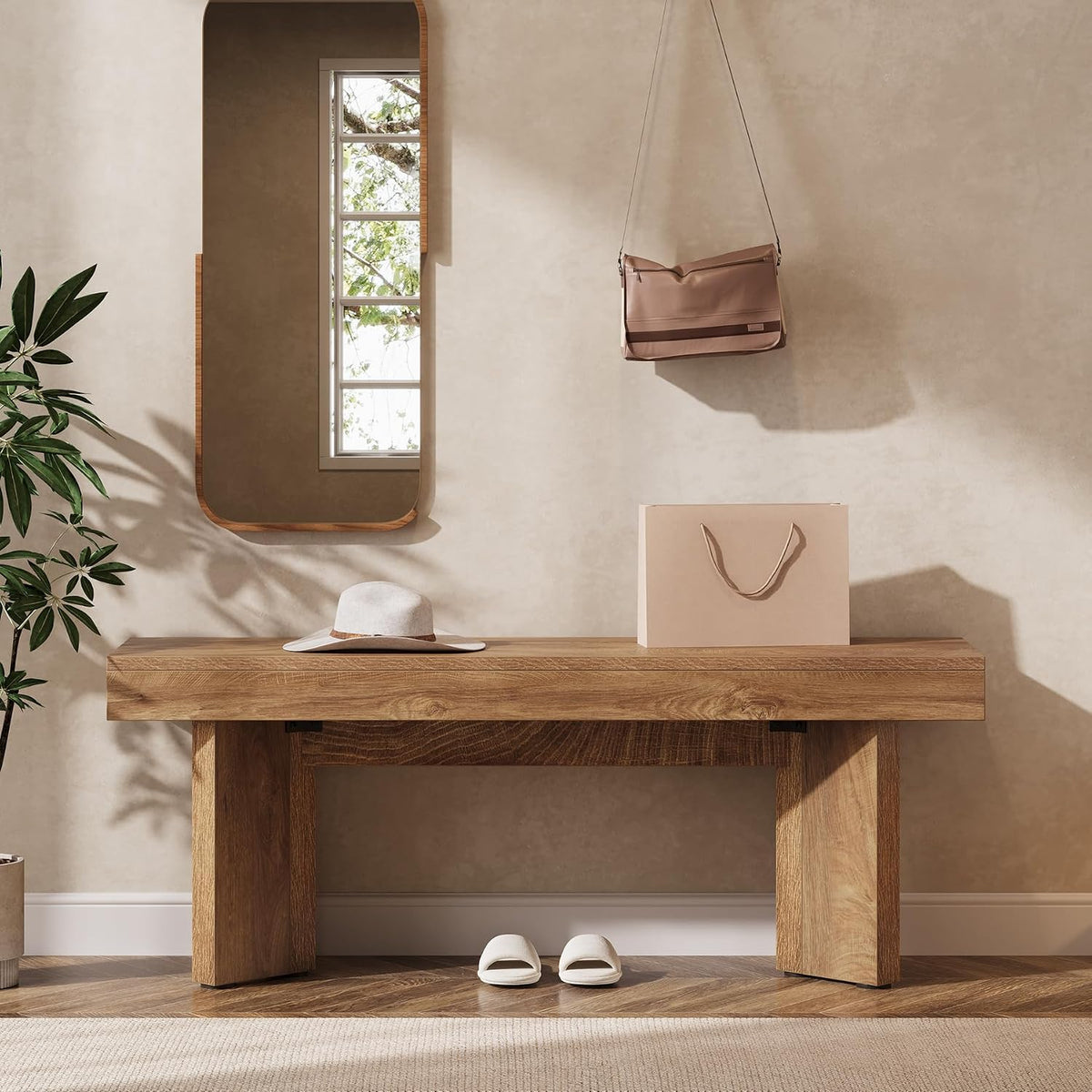 Rustic brown entryway bench under a wall mirror with a hat on top and slippers nearby