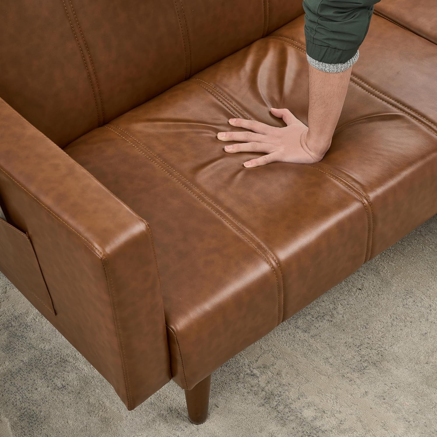 Close-up of brown PU seat cushion and armrest with a hand pressing into the padding