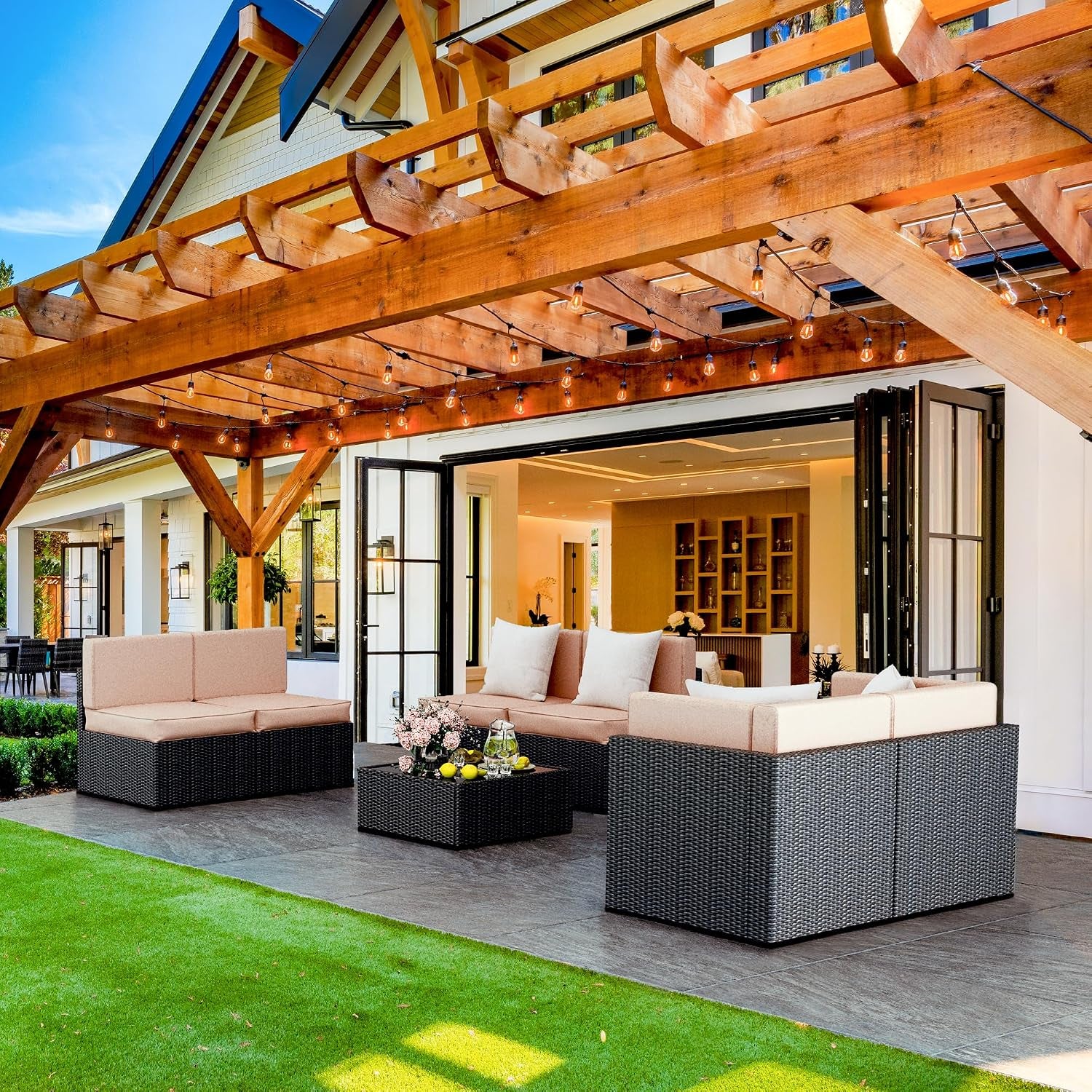 Patio beneath a wooden pergola showing rattan sectional pieces with beige cushions and a central coffee table.